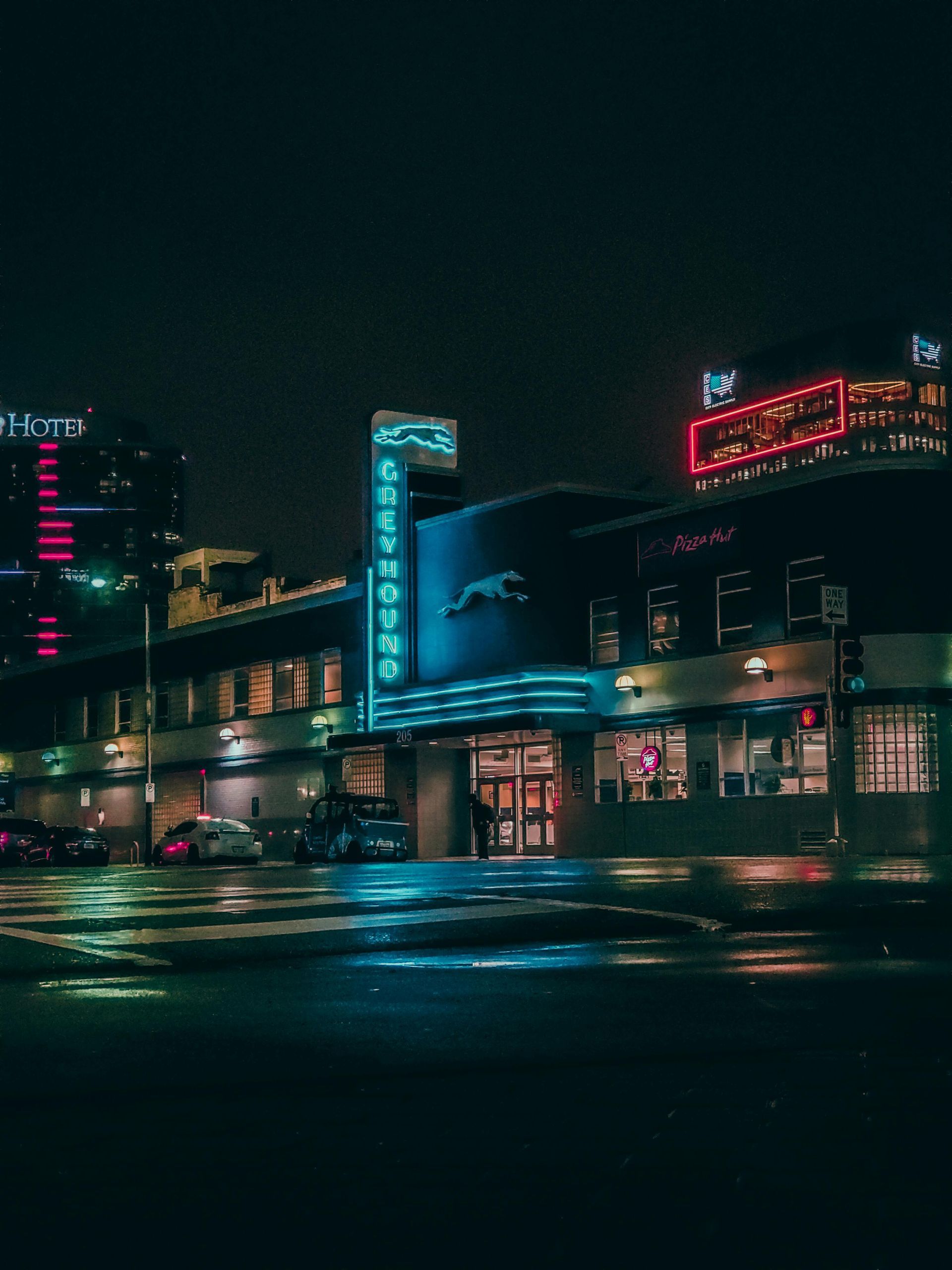 Greyhound bus station at night, illuminated by neon lights and city lights reflected on a wet street.