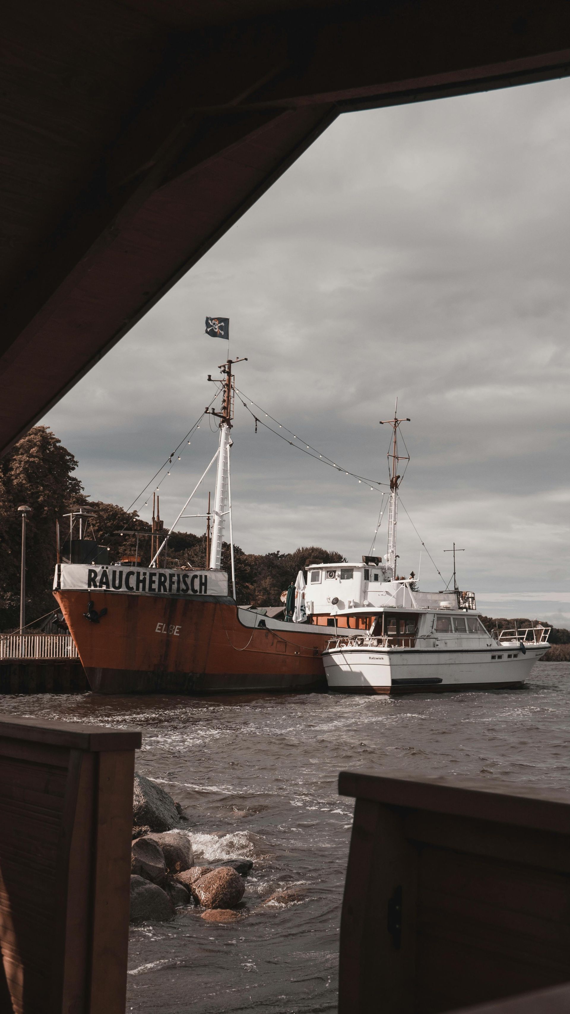 Orange and white boats docked at a pier under a cloudy sky.