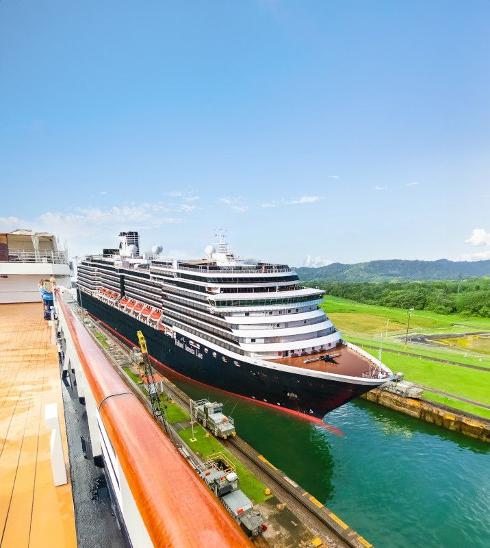 Cruise ship in a canal, green water and vegetation, blue sky, white and black vessel.