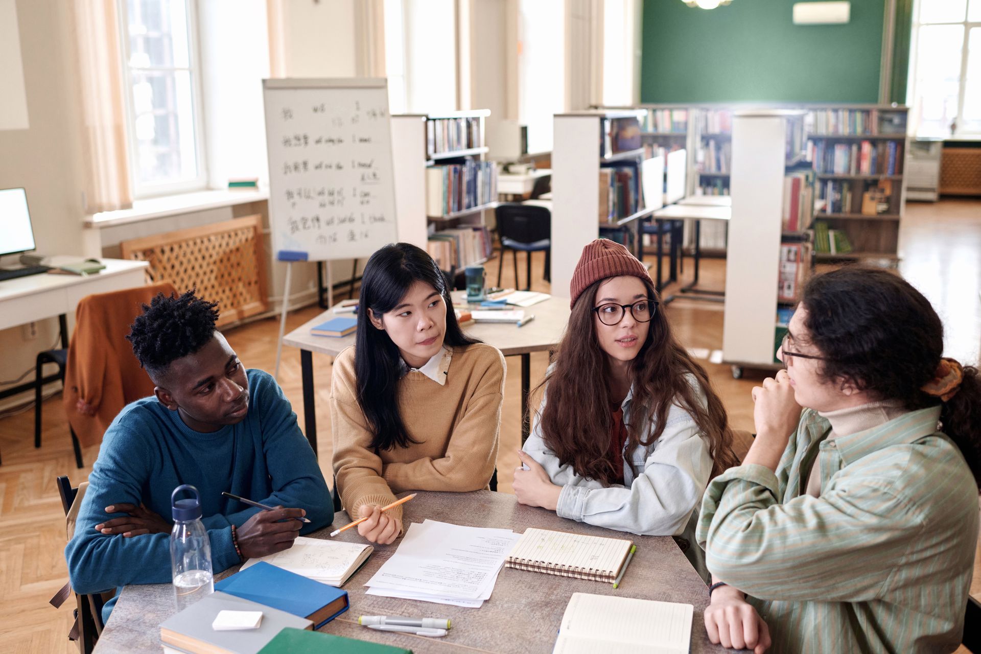 A group of young people are sitting around a table in a library.