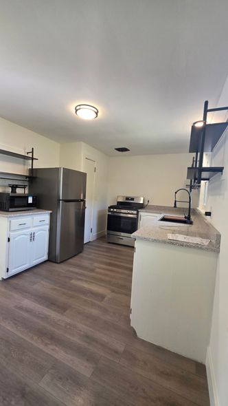 A small kitchen with white cabinets, stainless steel appliances, and wood-look flooring.