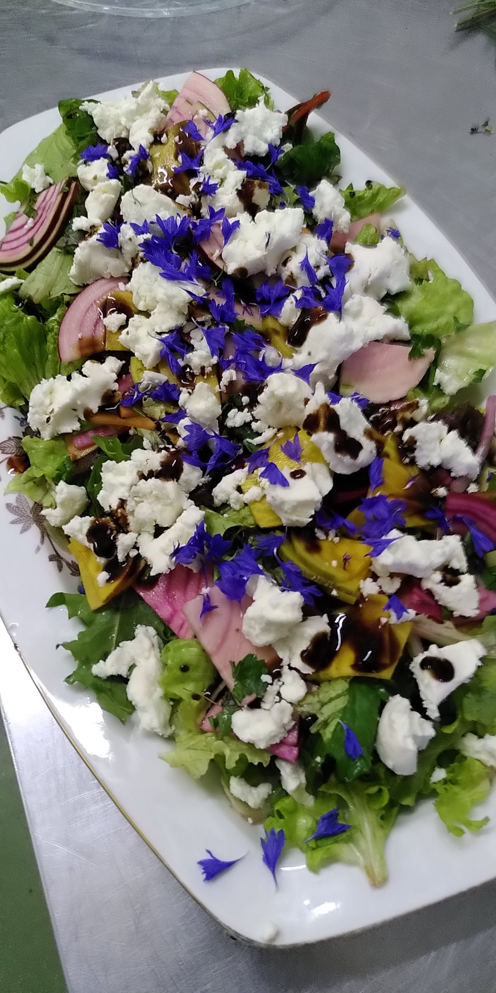 Een wit bord met daarop een salade en blauwe eetbare bloemen.