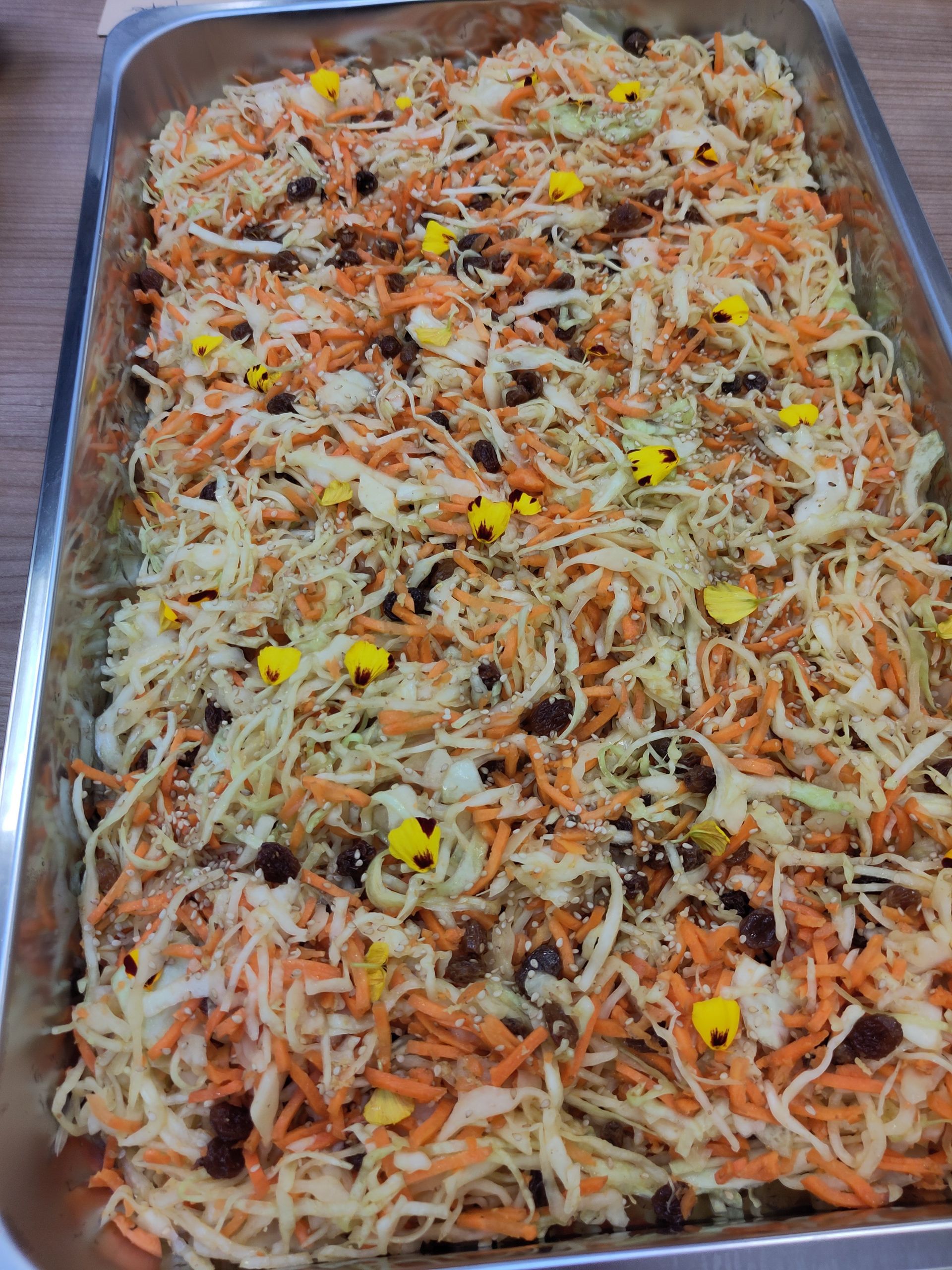 Een schaal met koolsalade met wortelen, maïs en rozijnen op tafel.