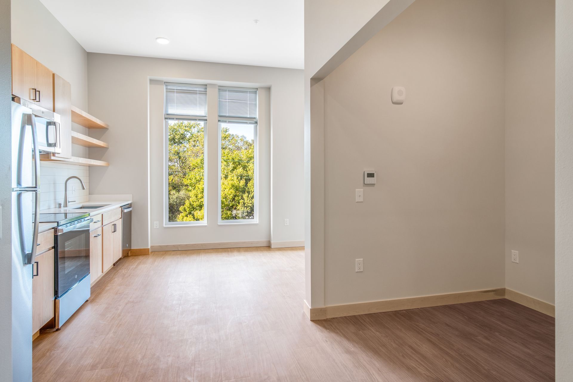 An empty apartment with a kitchen , dining room , and living room.