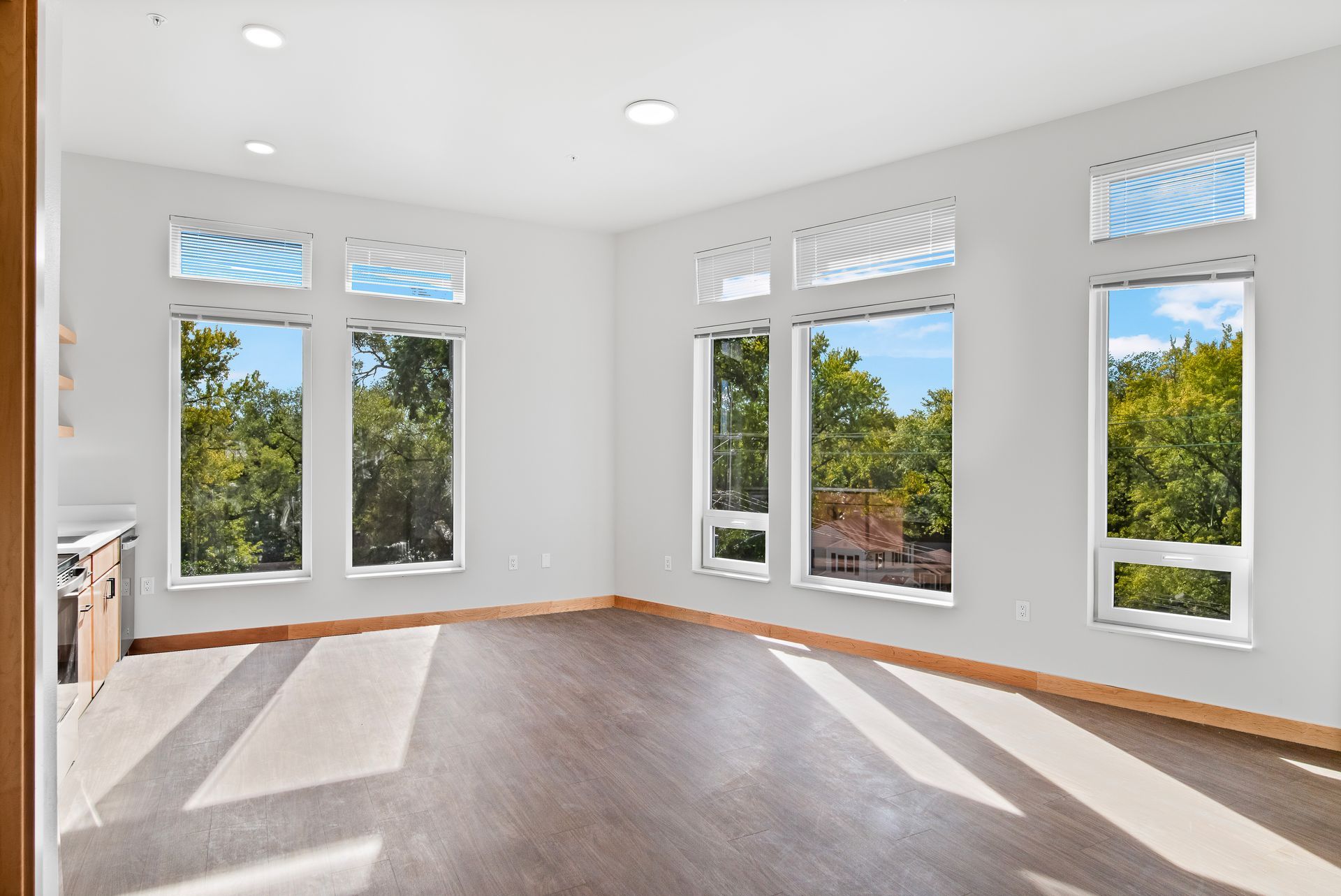 An empty living room with lots of windows and hardwood floors.