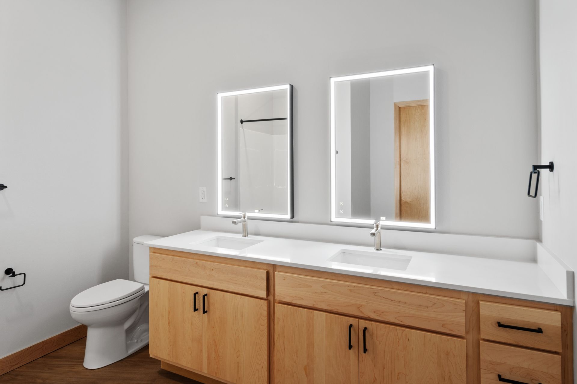 A bathroom with two sinks , a toilet , and two mirrors.
