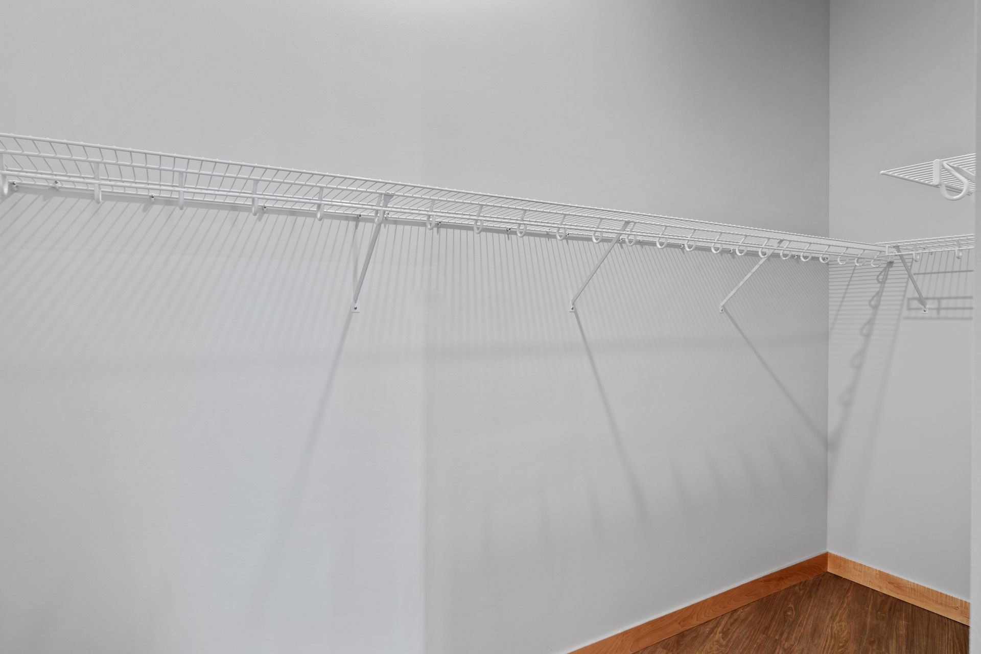 An empty walk in closet with white wire shelves and a wooden floor.