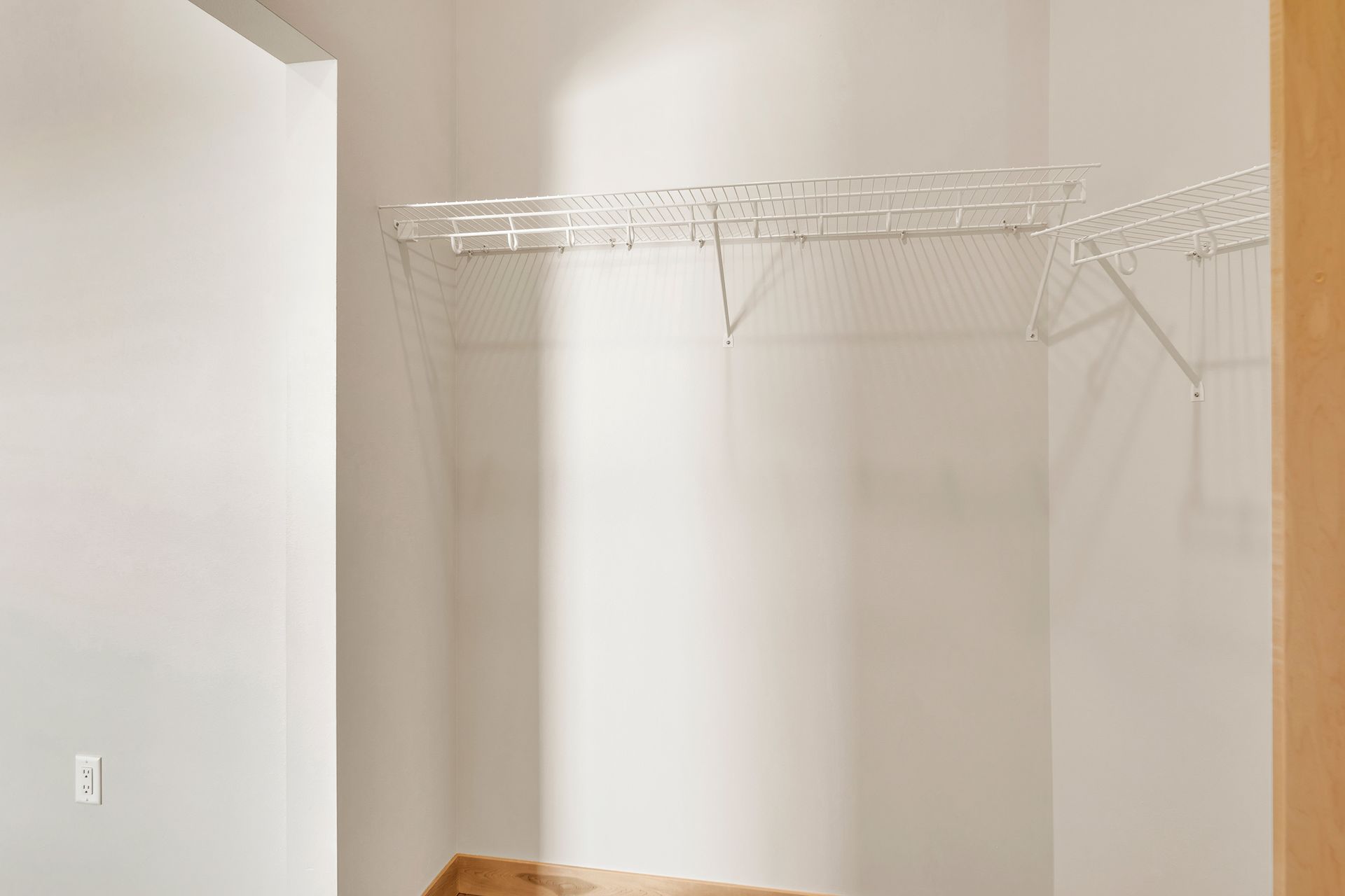 An empty walk in closet with a wooden floor and white walls.