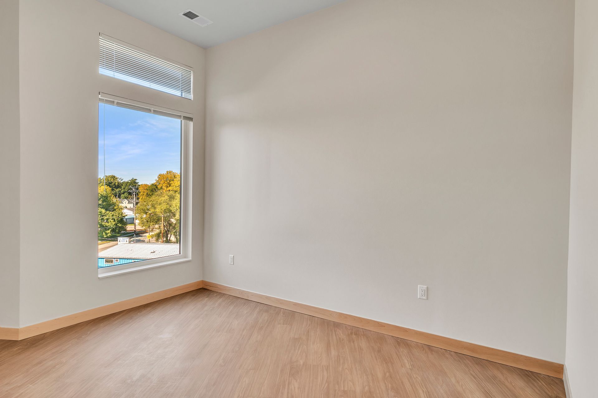 An empty room with a large window and hardwood floors.