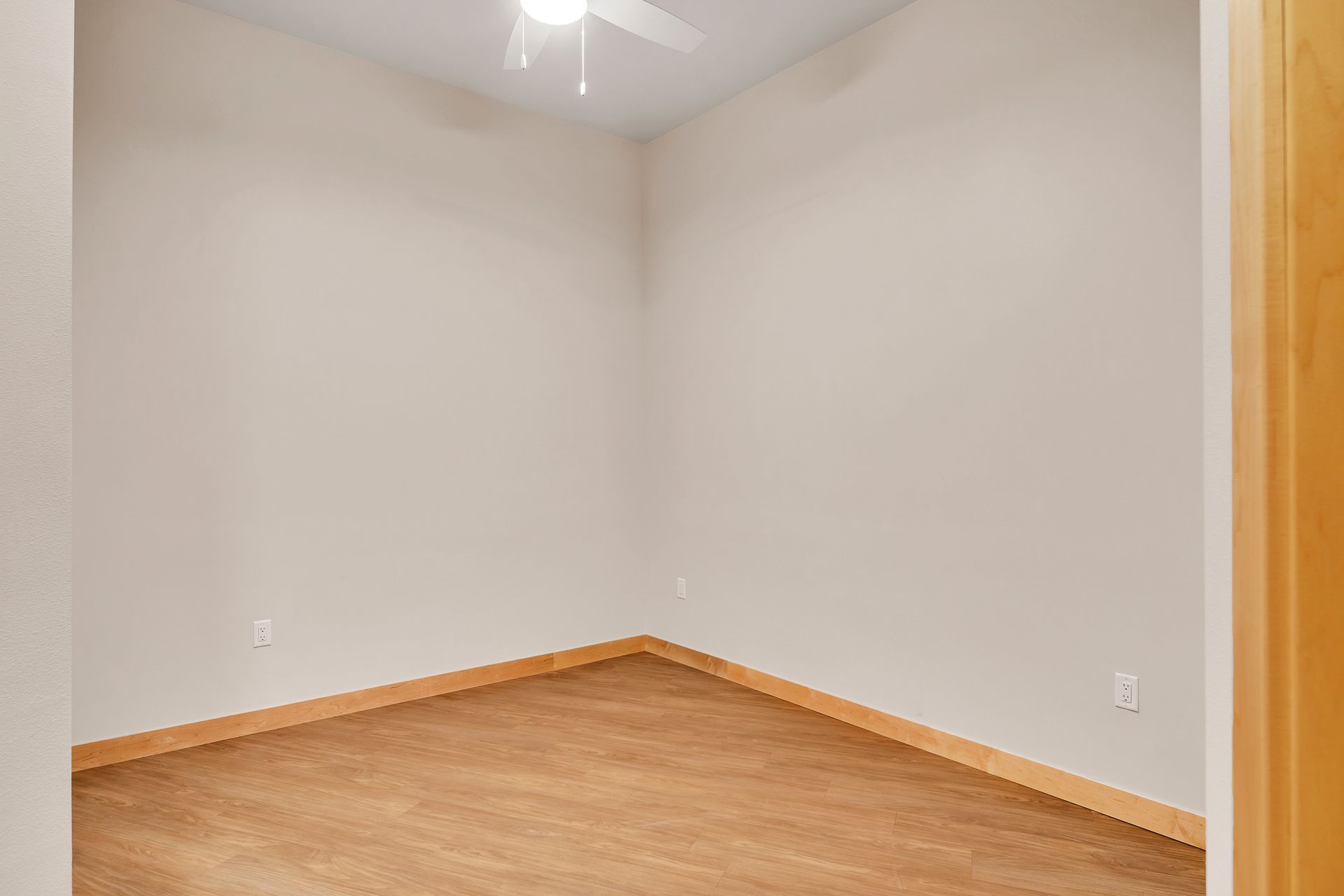 An empty room with a ceiling fan and a wooden floor.