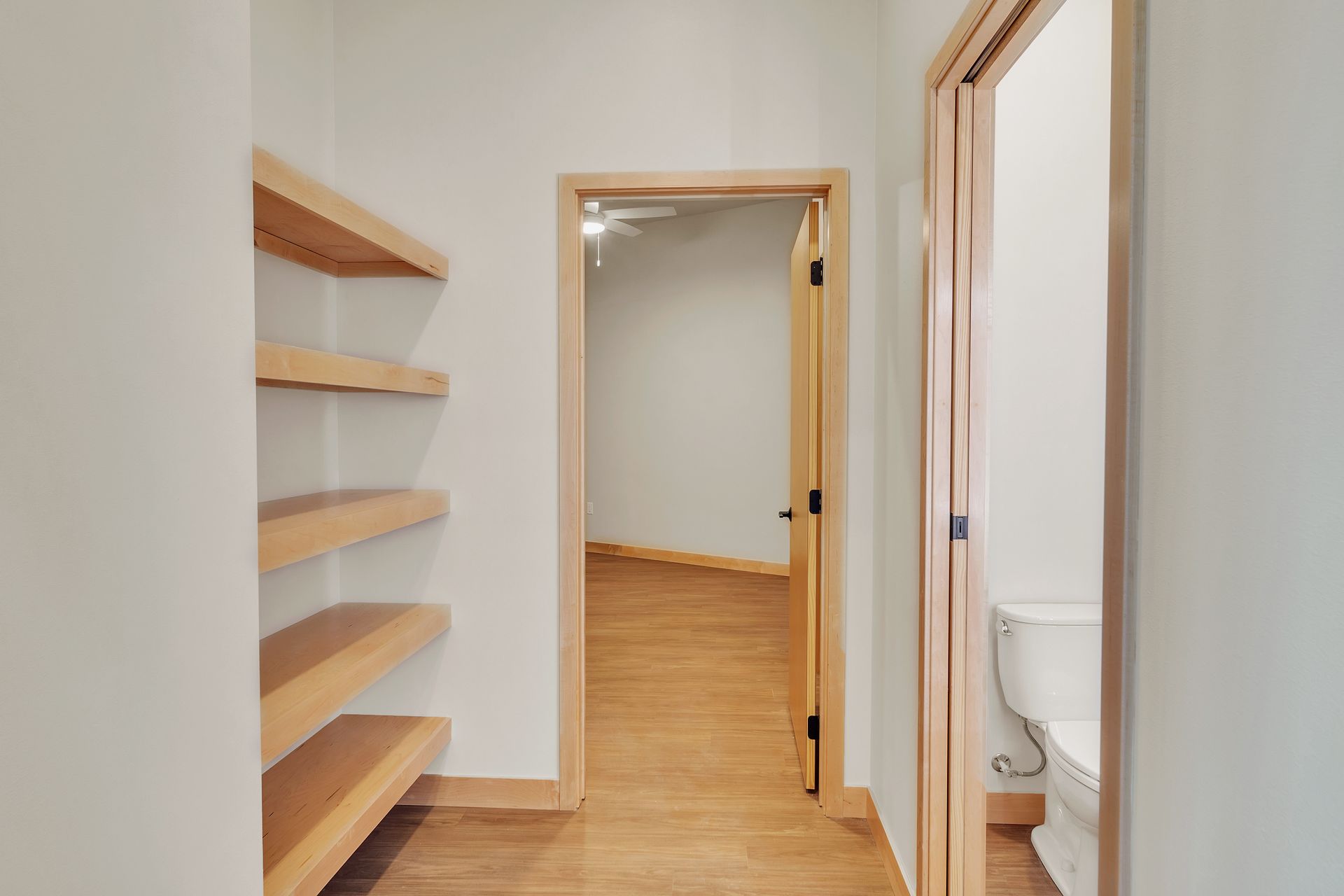 A hallway leading to a bathroom with a toilet and shelves.