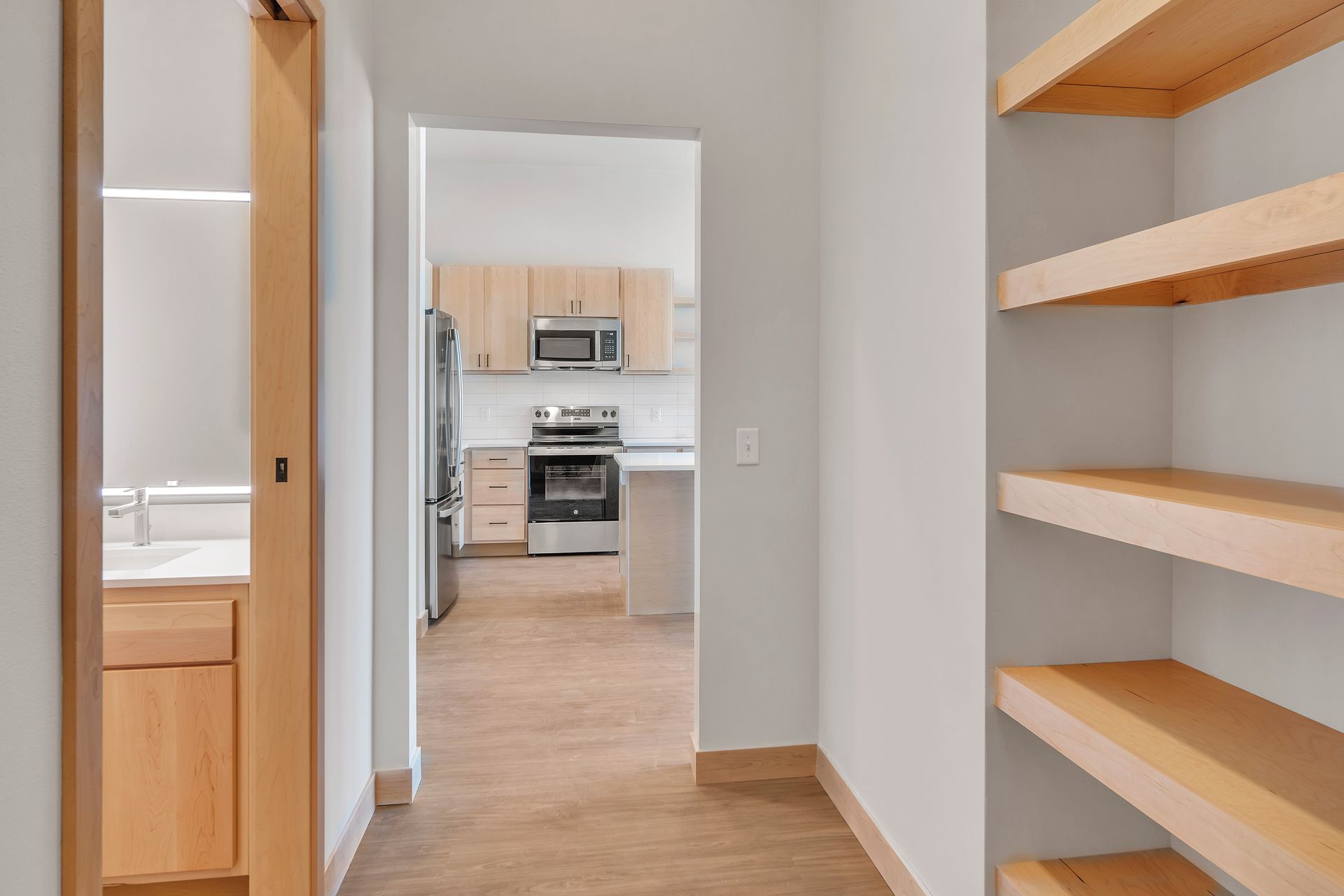 A hallway with wooden shelves leading to a kitchen.