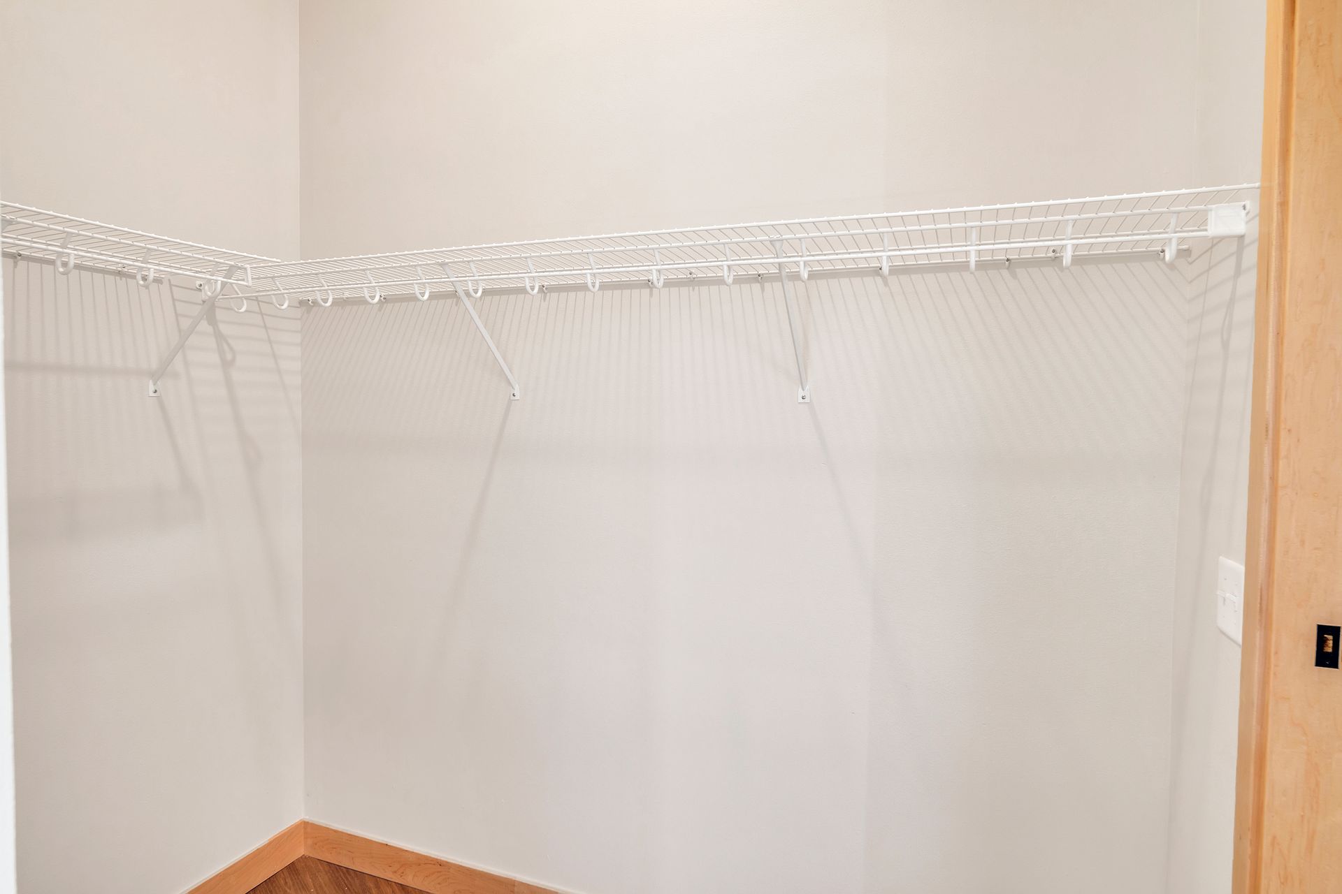 An empty walk in closet with white shelves and a wooden floor.