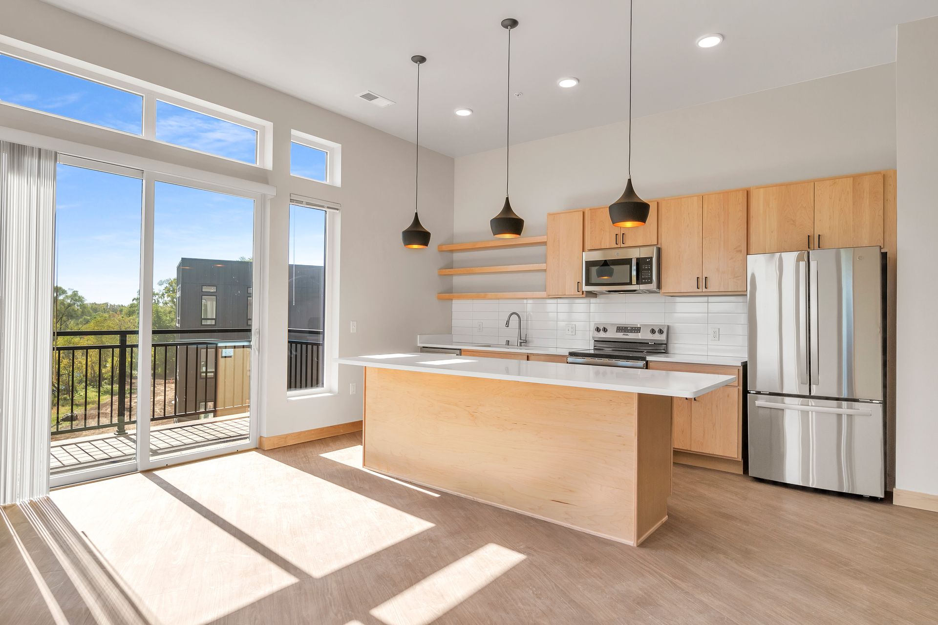 A kitchen with a large island , stainless steel appliances , wooden cabinets and a sliding glass door.