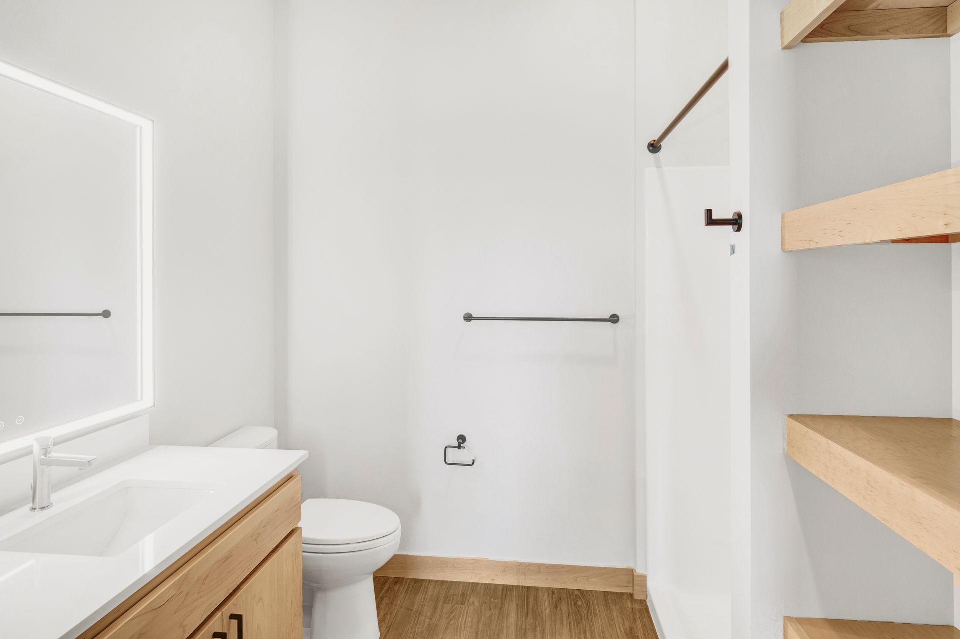 A bathroom with a toilet , sink , mirror and shelves.