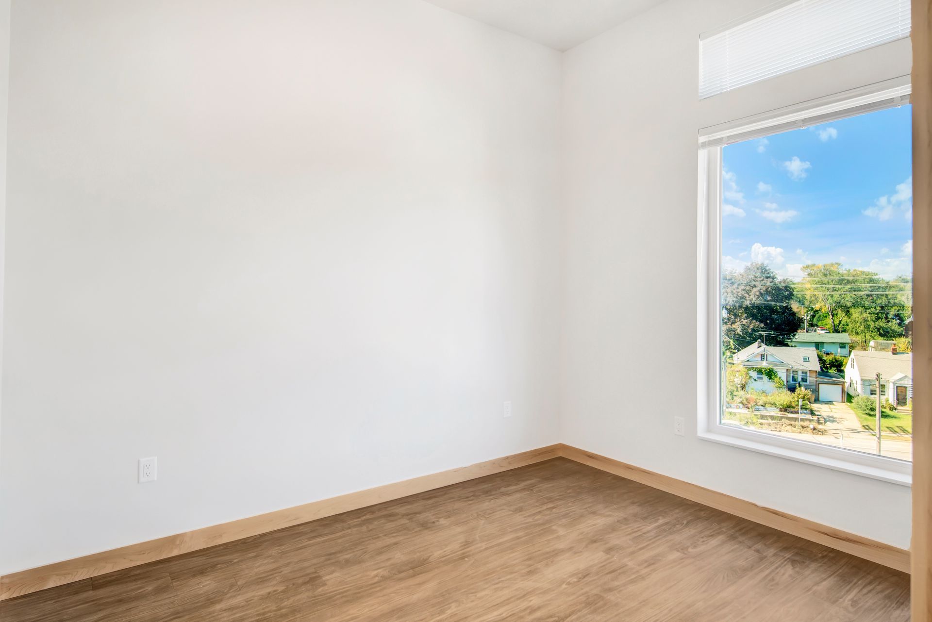 An empty room with a large window and wooden floors.