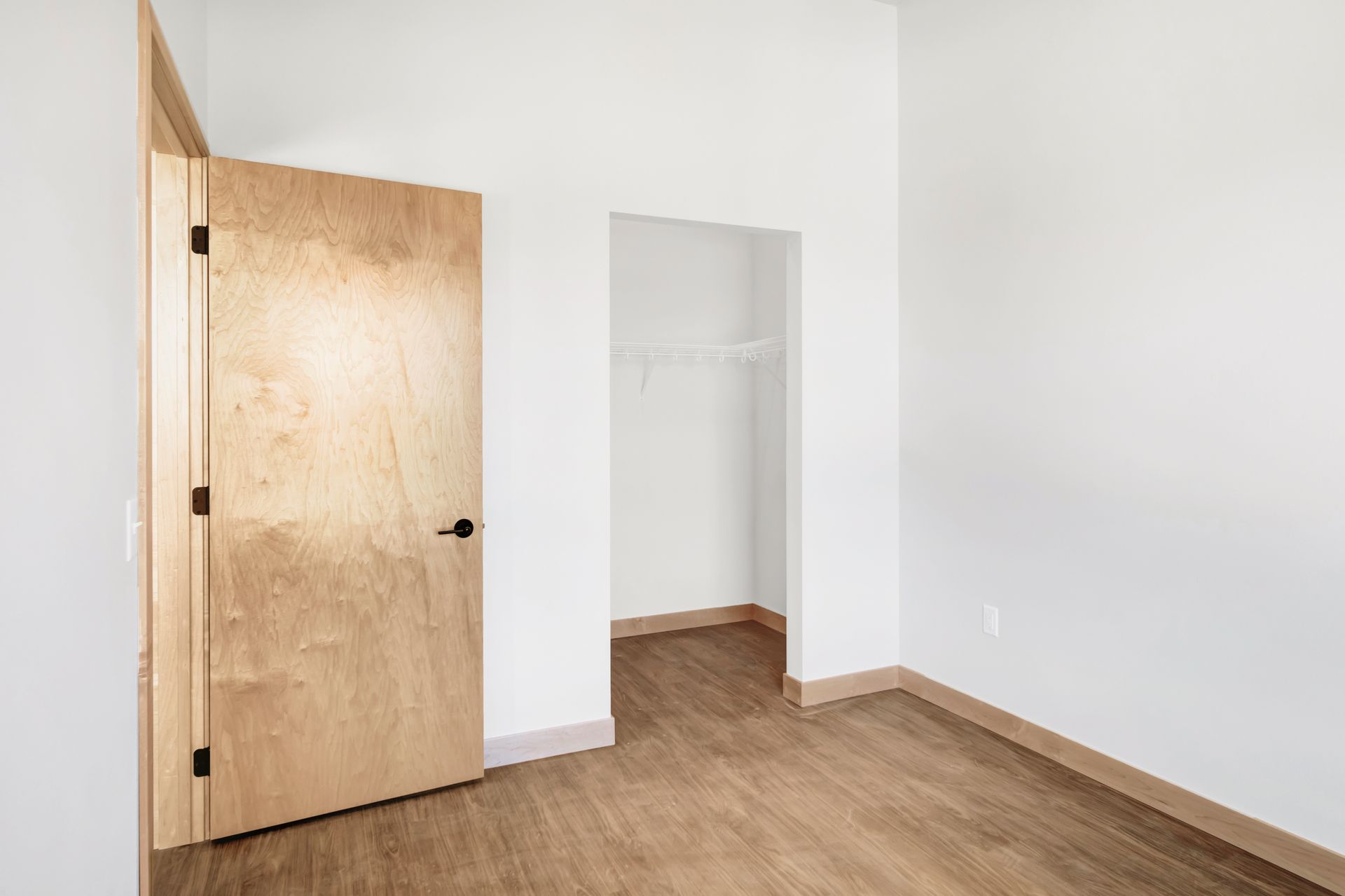 An empty bedroom with a wooden floor and a wooden door leading to a closet.