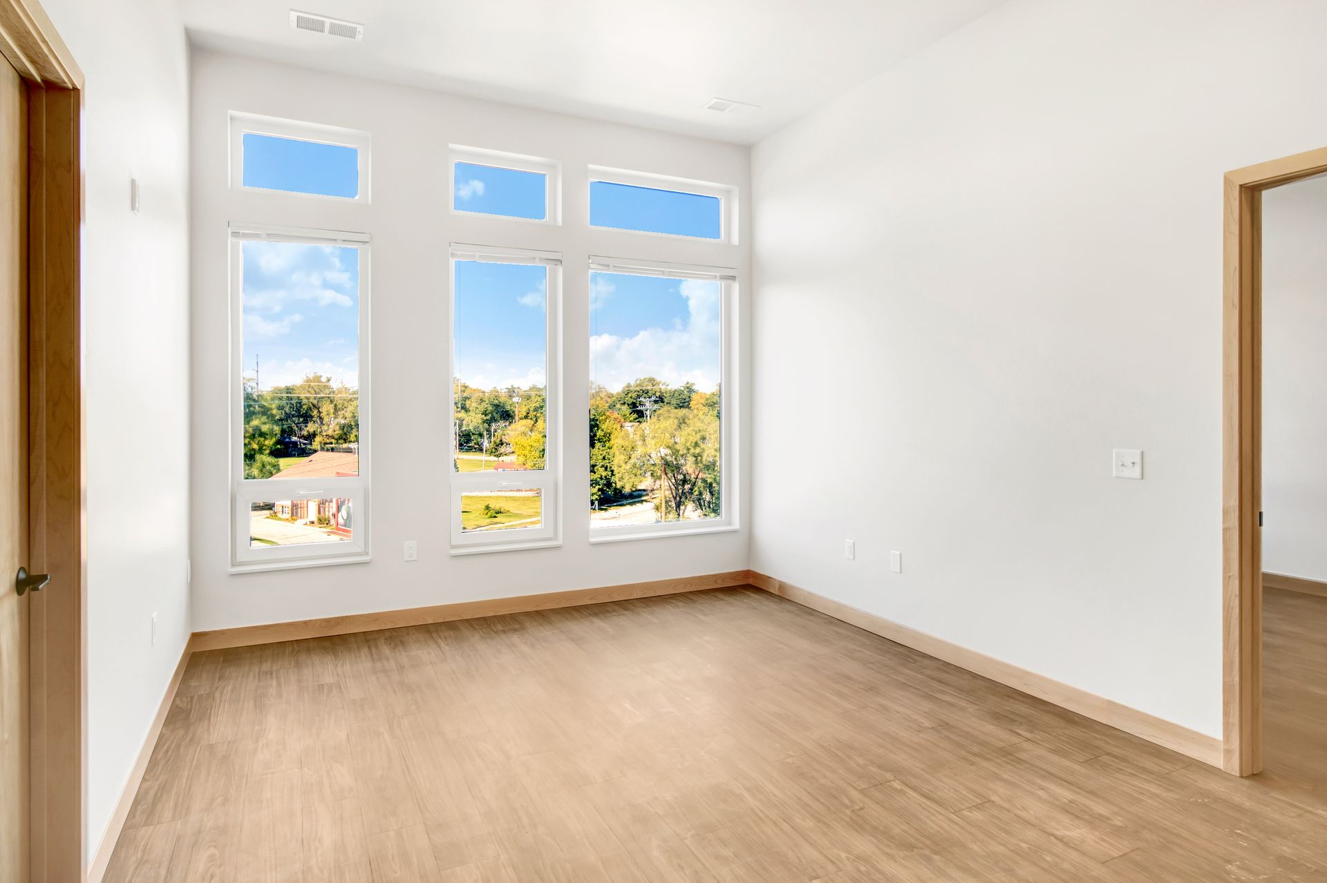 An empty room with hardwood floors and three windows.