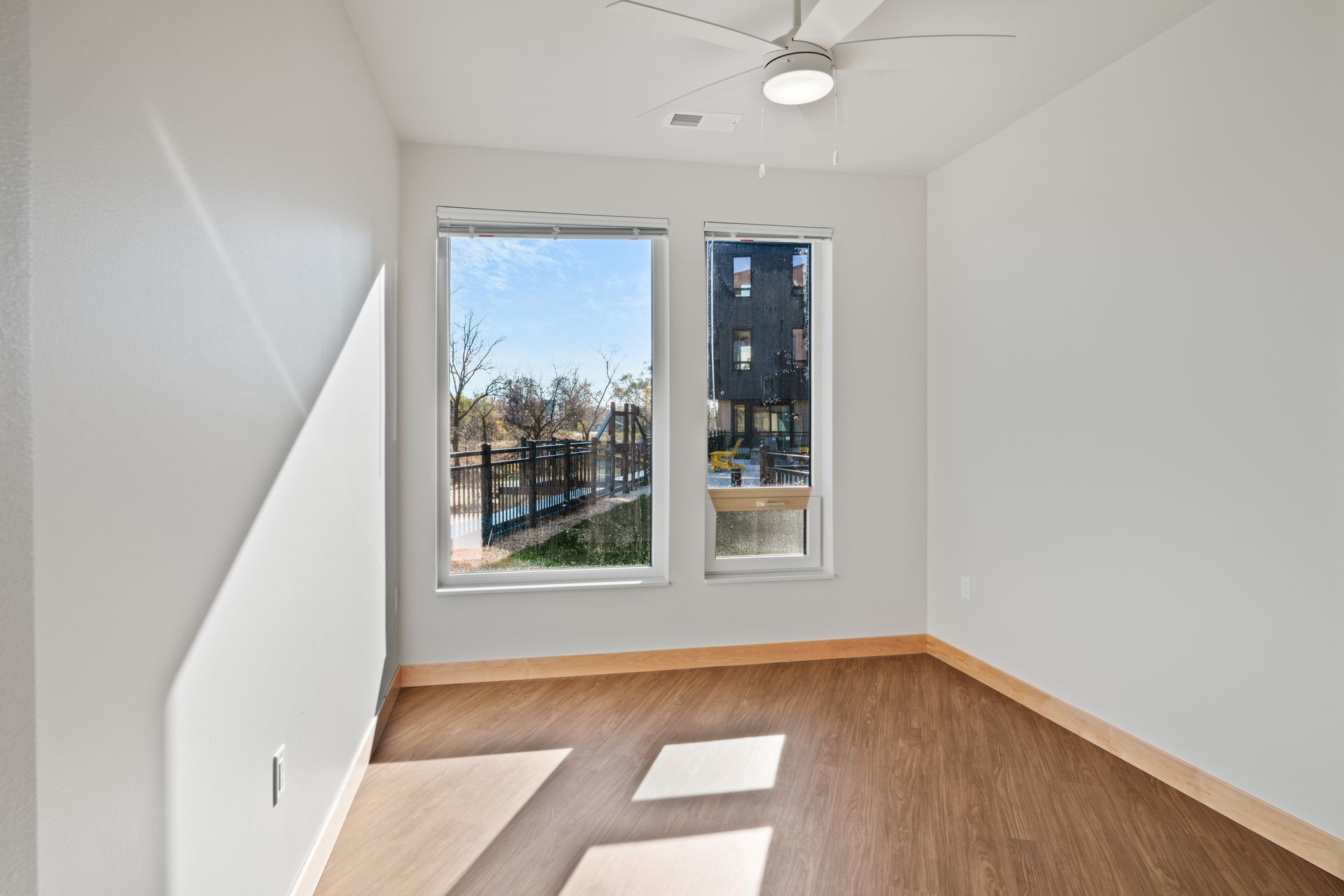 An empty room with a ceiling fan and two windows.