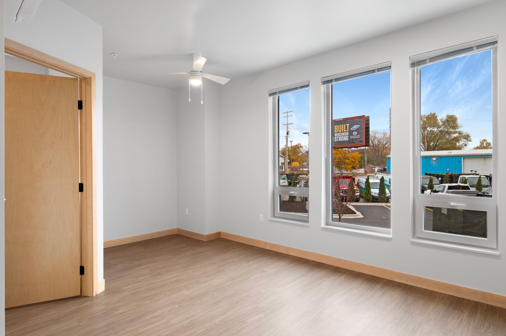 An empty room with three windows and a ceiling fan.