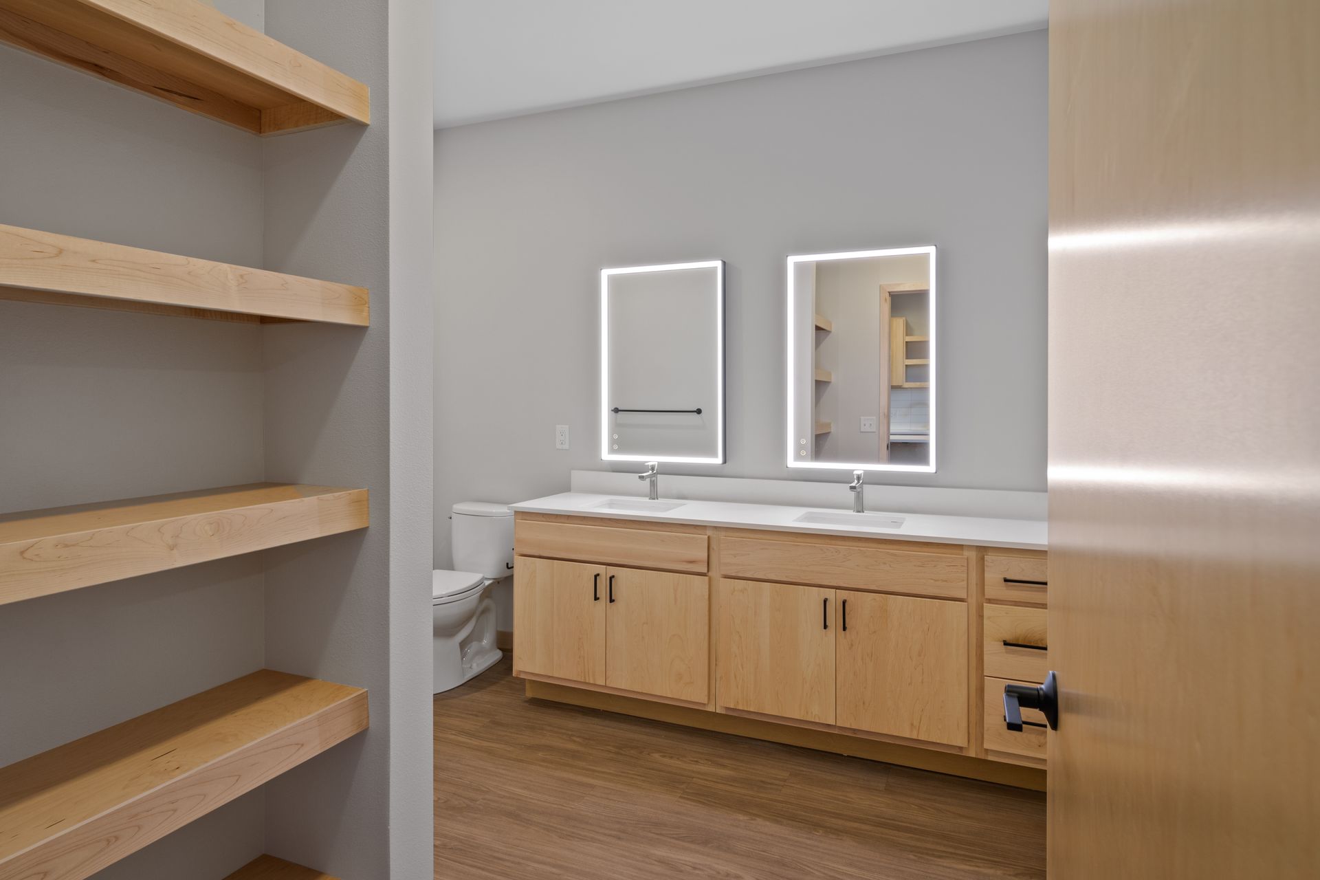 A bathroom with two sinks , two led mirrors and a toilet.