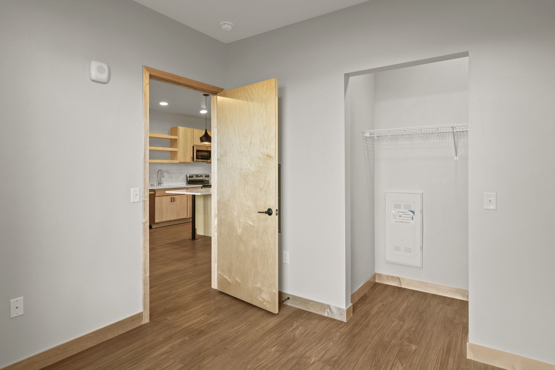 An empty room with a lvp floor and a door leading to a kitchen.