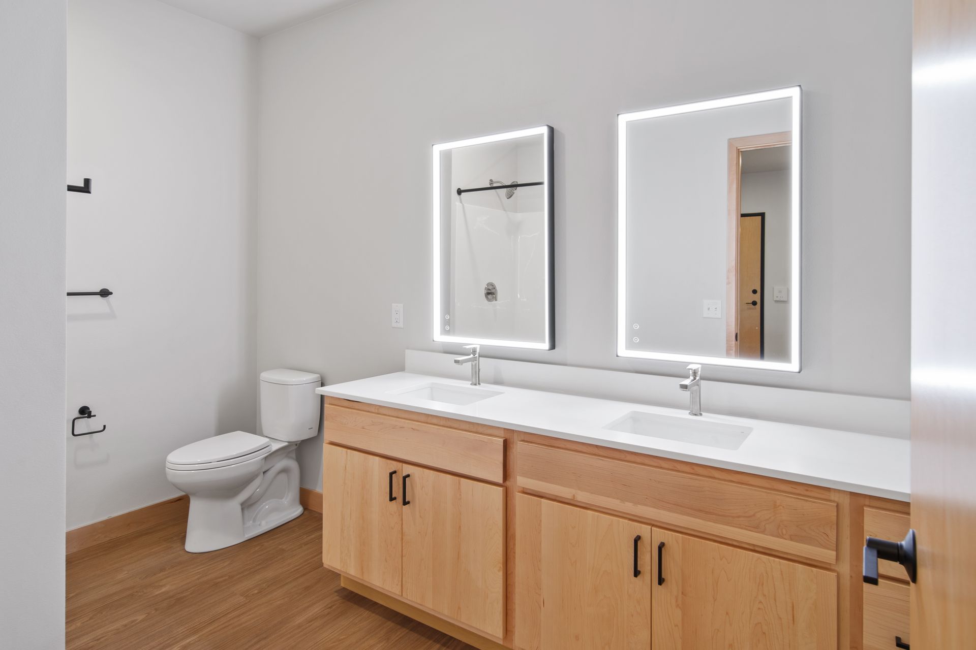 A bathroom with two sinks , a toilet , and two led mirrors.