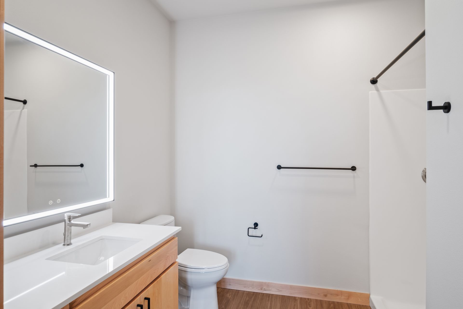 A bathroom with a toilet , sink , led mirror and shower.