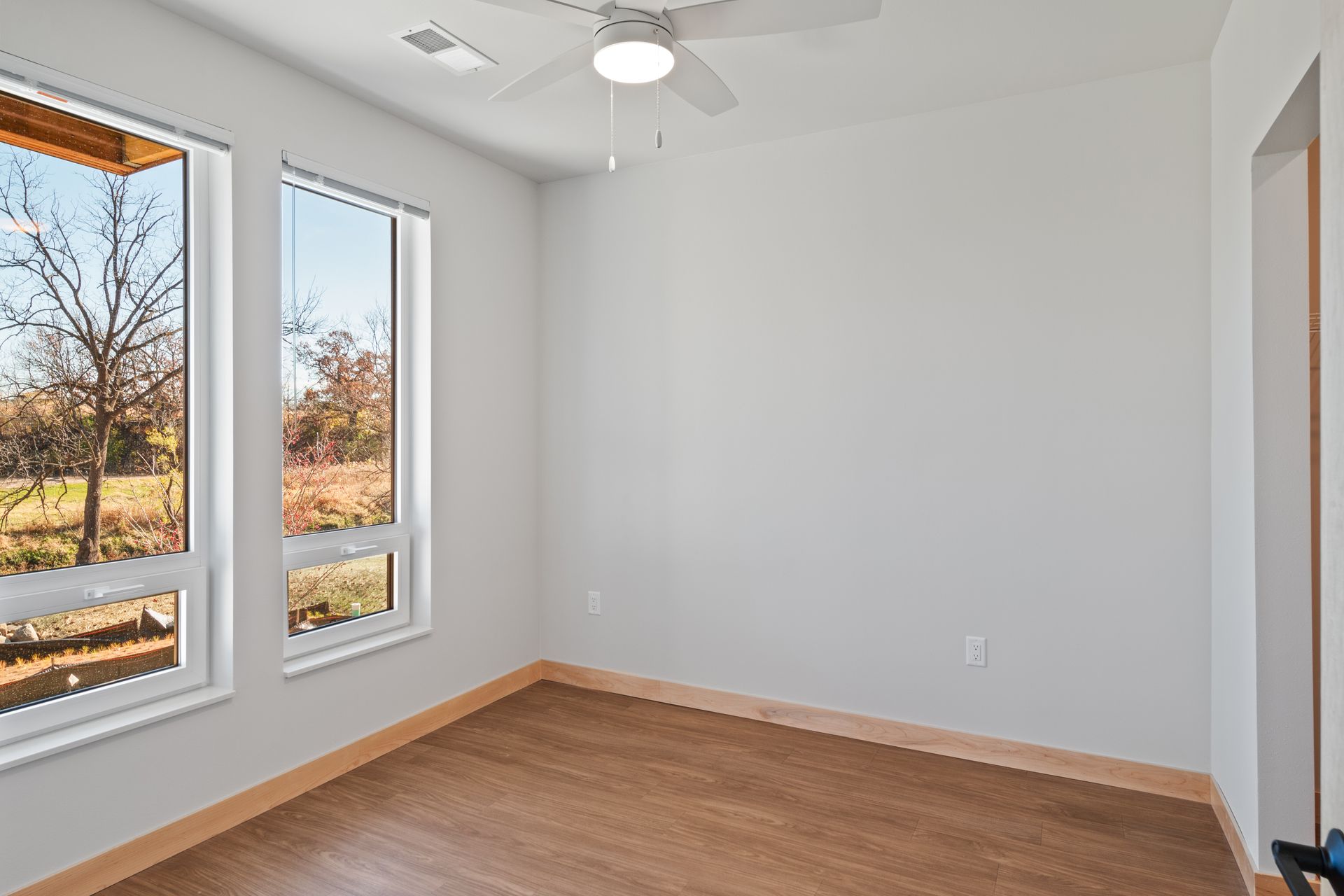 An empty room with a ceiling fan and two windows.