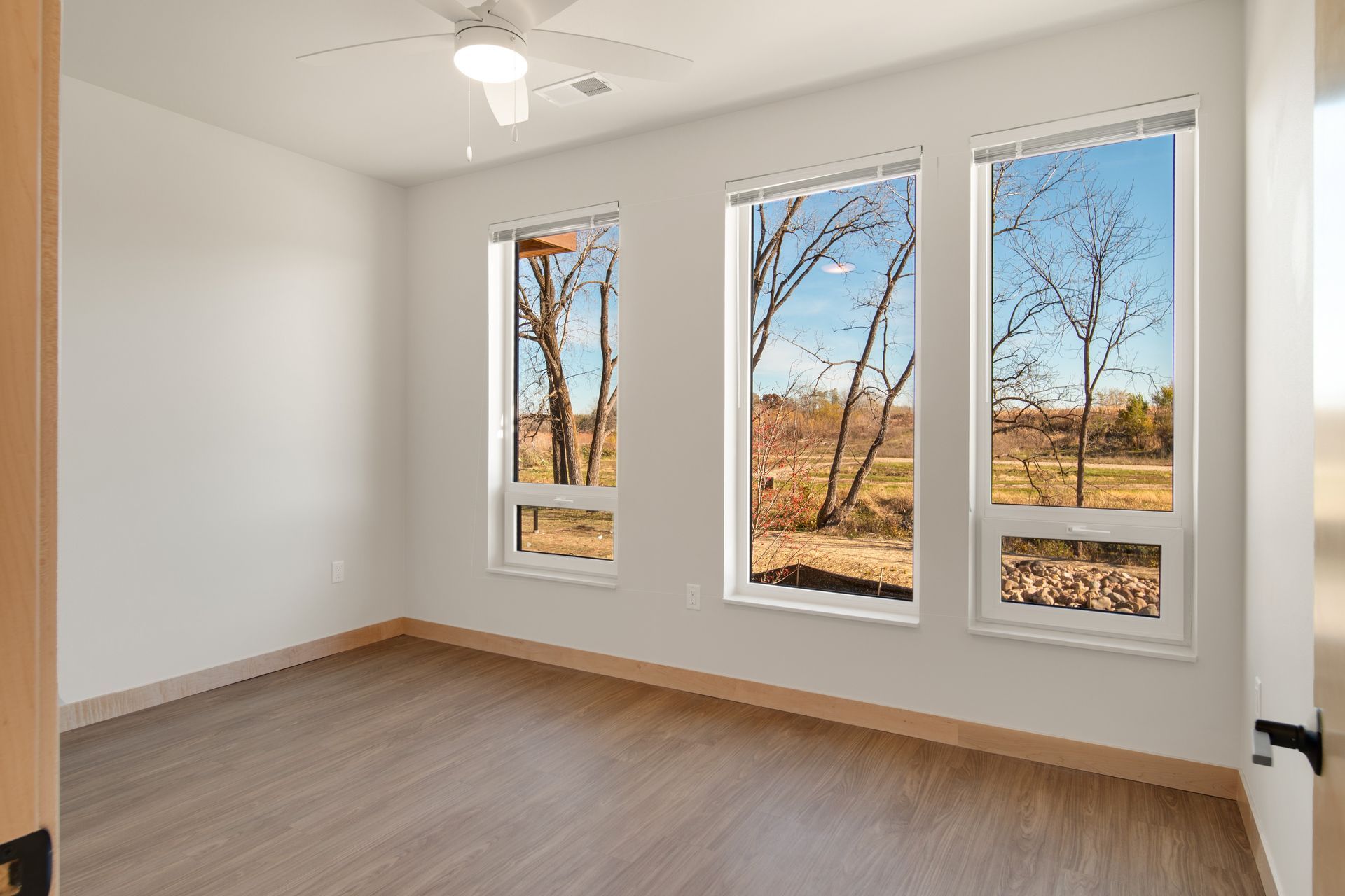 An empty bedroom with three windows and a ceiling fan.