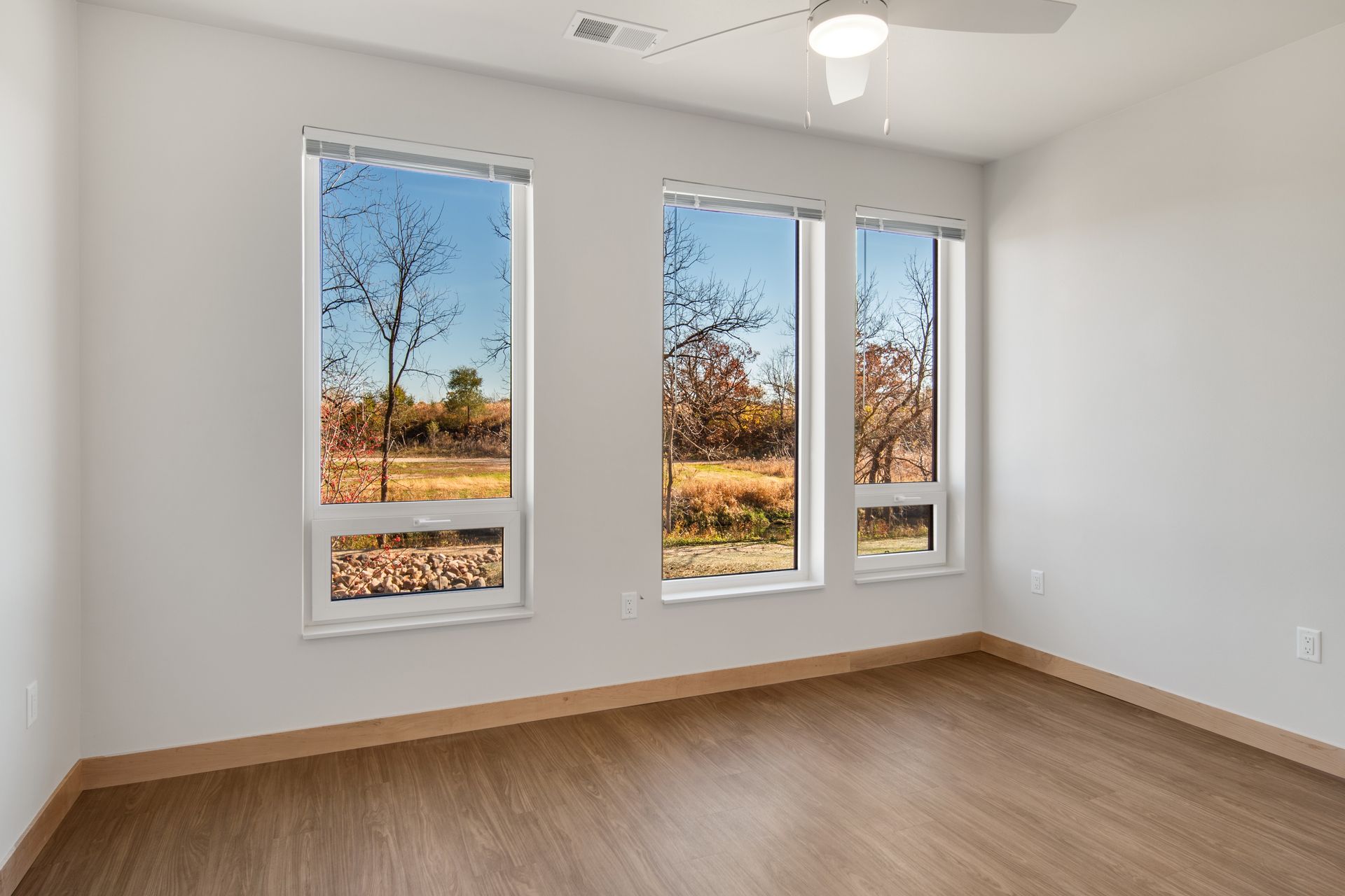 An empty bedroom with three windows and a ceiling fan.