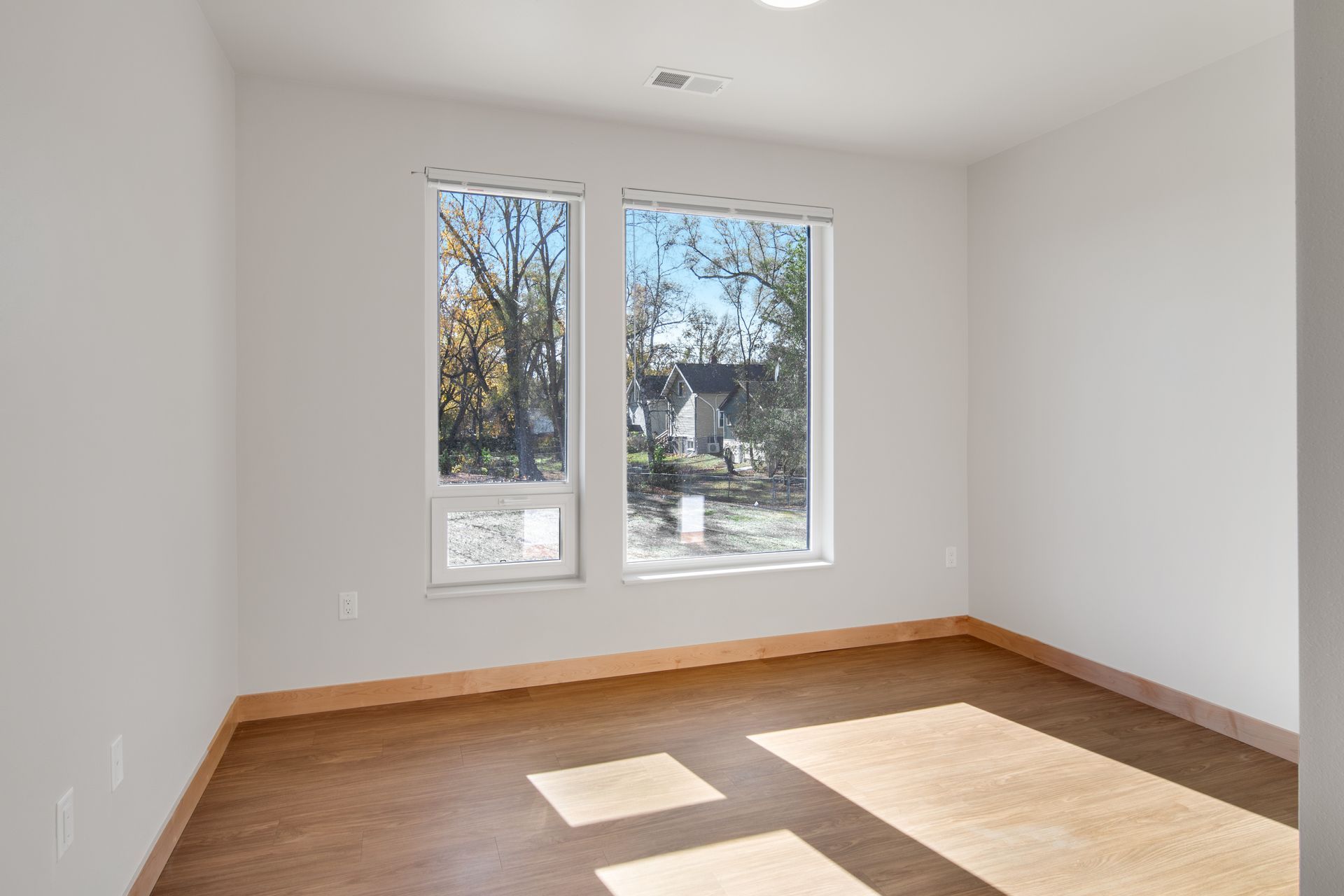 An empty room with two windows and a wooden floor.