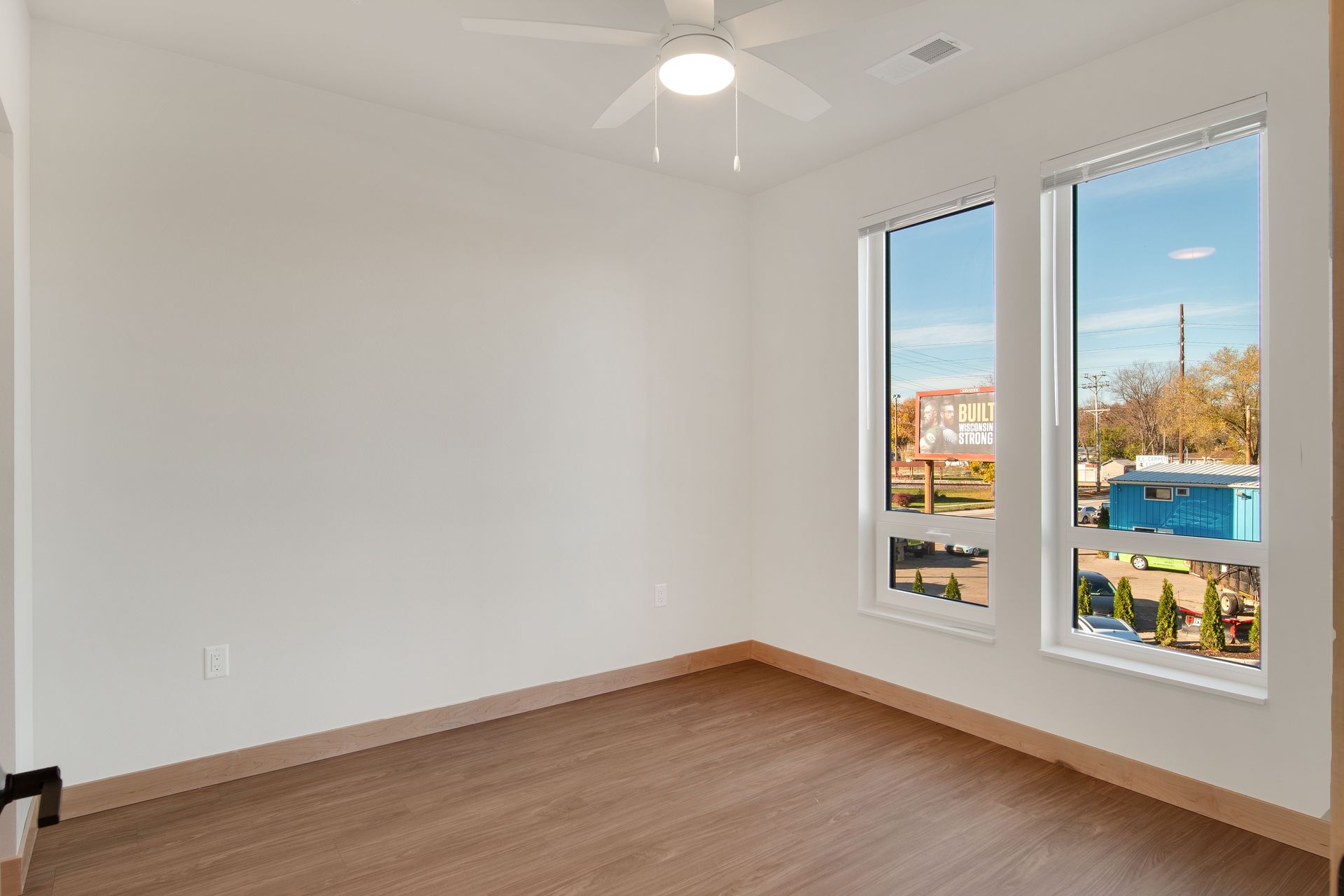 An empty room with two windows and a ceiling fan.