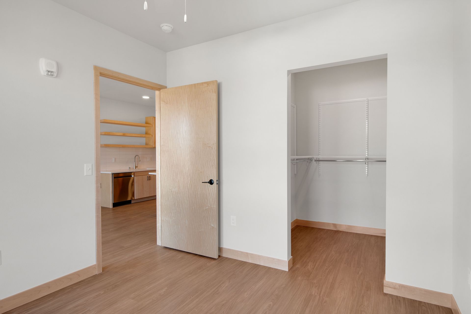 An empty room with a closet and a door leading to a kitchen.