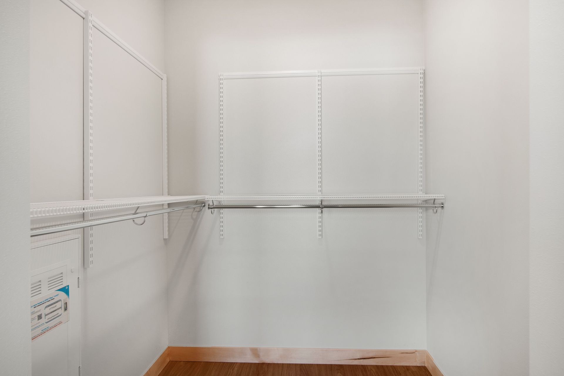 An empty walk in closet with a wooden floor and white shelves.