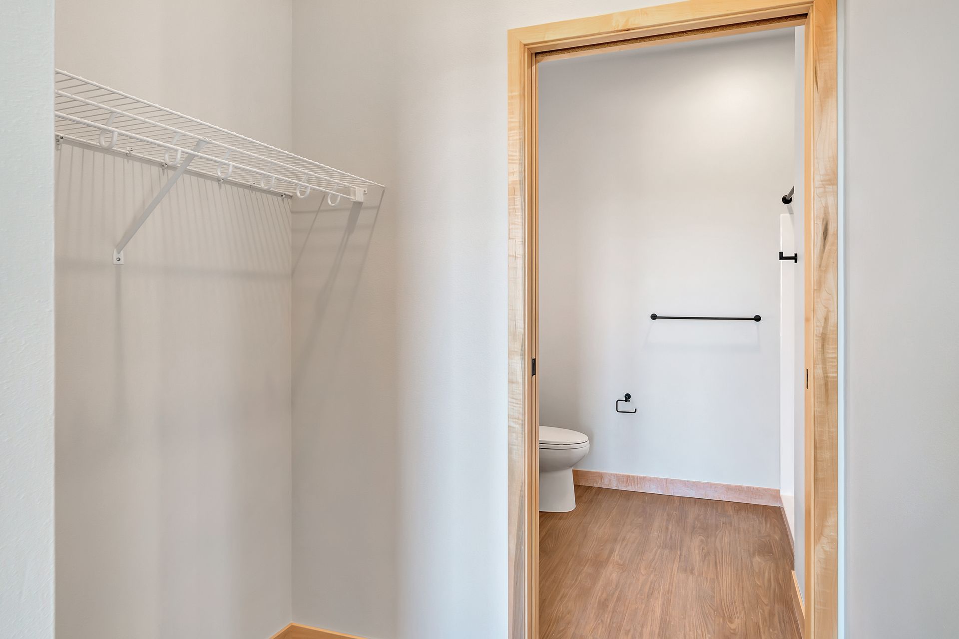A walk in closet with a toilet and a wooden floor.