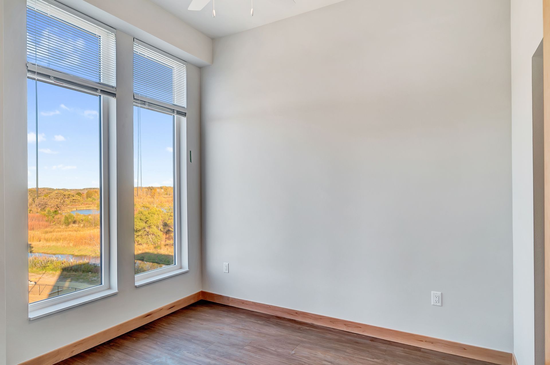 An empty room with two large windows and a ceiling fan.