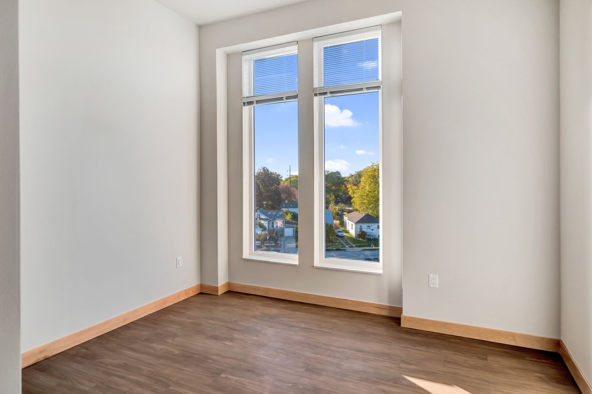 An empty room with two windows and a wooden floor.