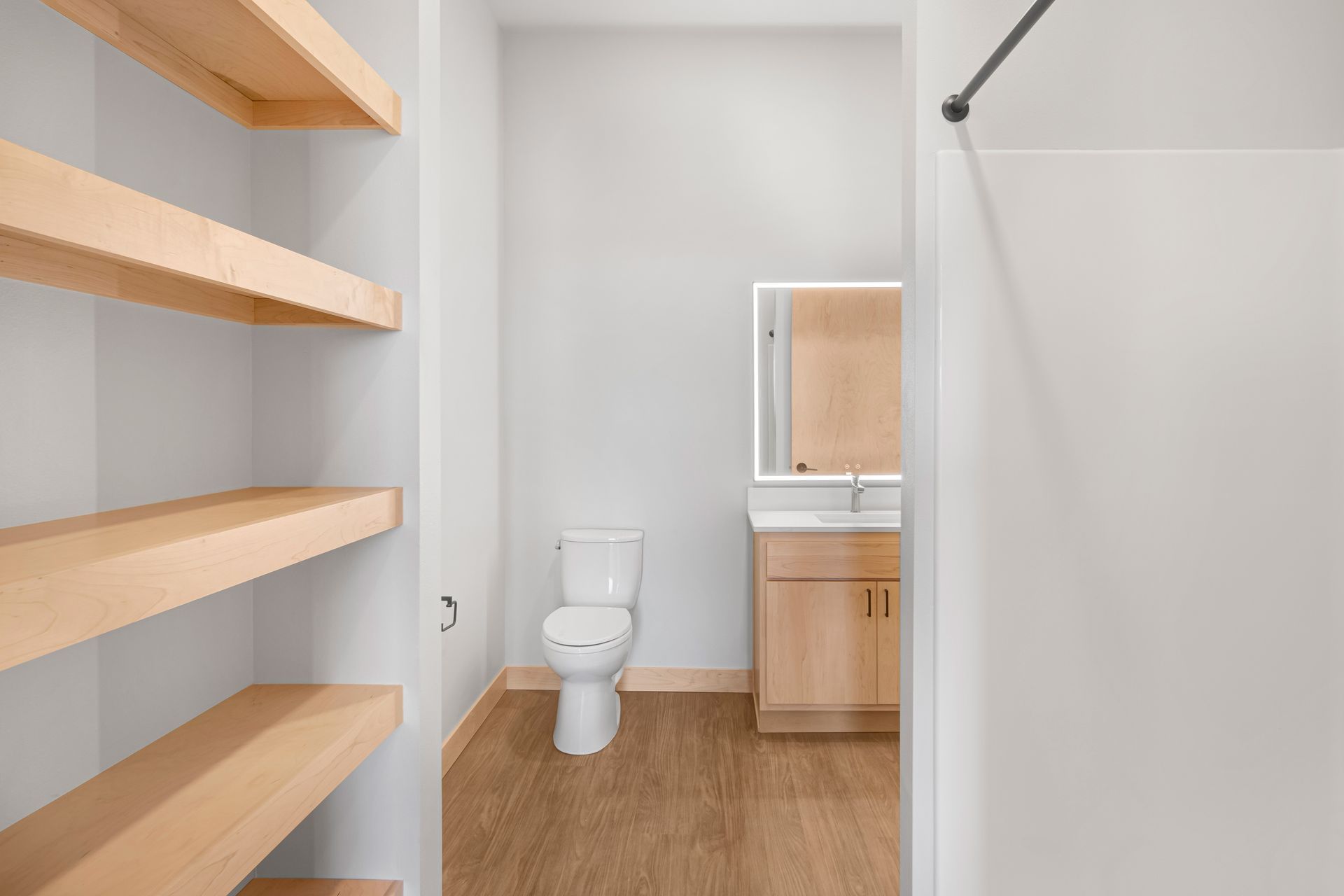 A bathroom with a toilet , sink , mirror and wooden shelves.