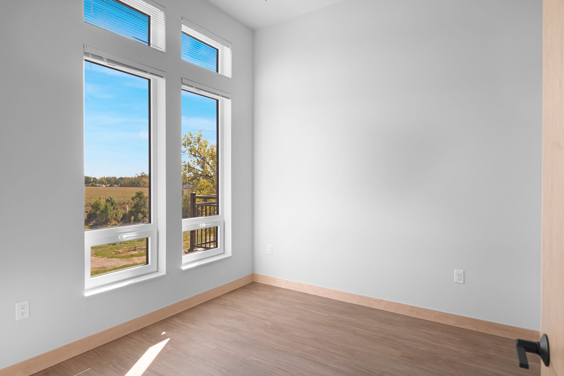 An empty room with two windows and a wooden floor.