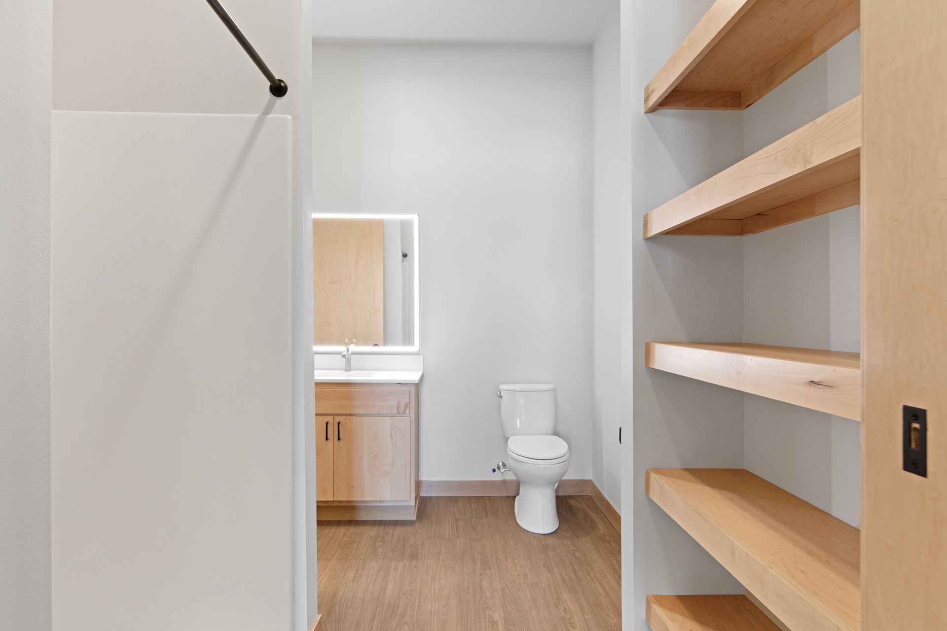 A bathroom with a toilet , sink , mirror and shelves.