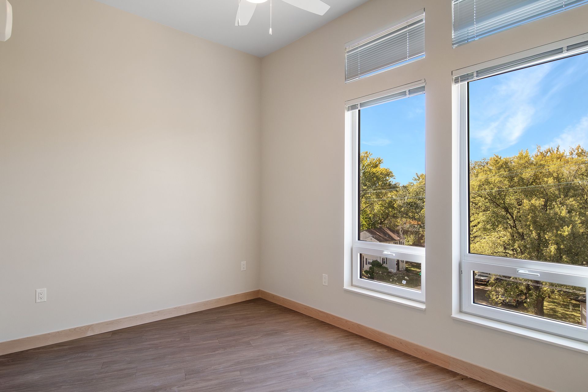 An empty room with two windows and a ceiling fan.