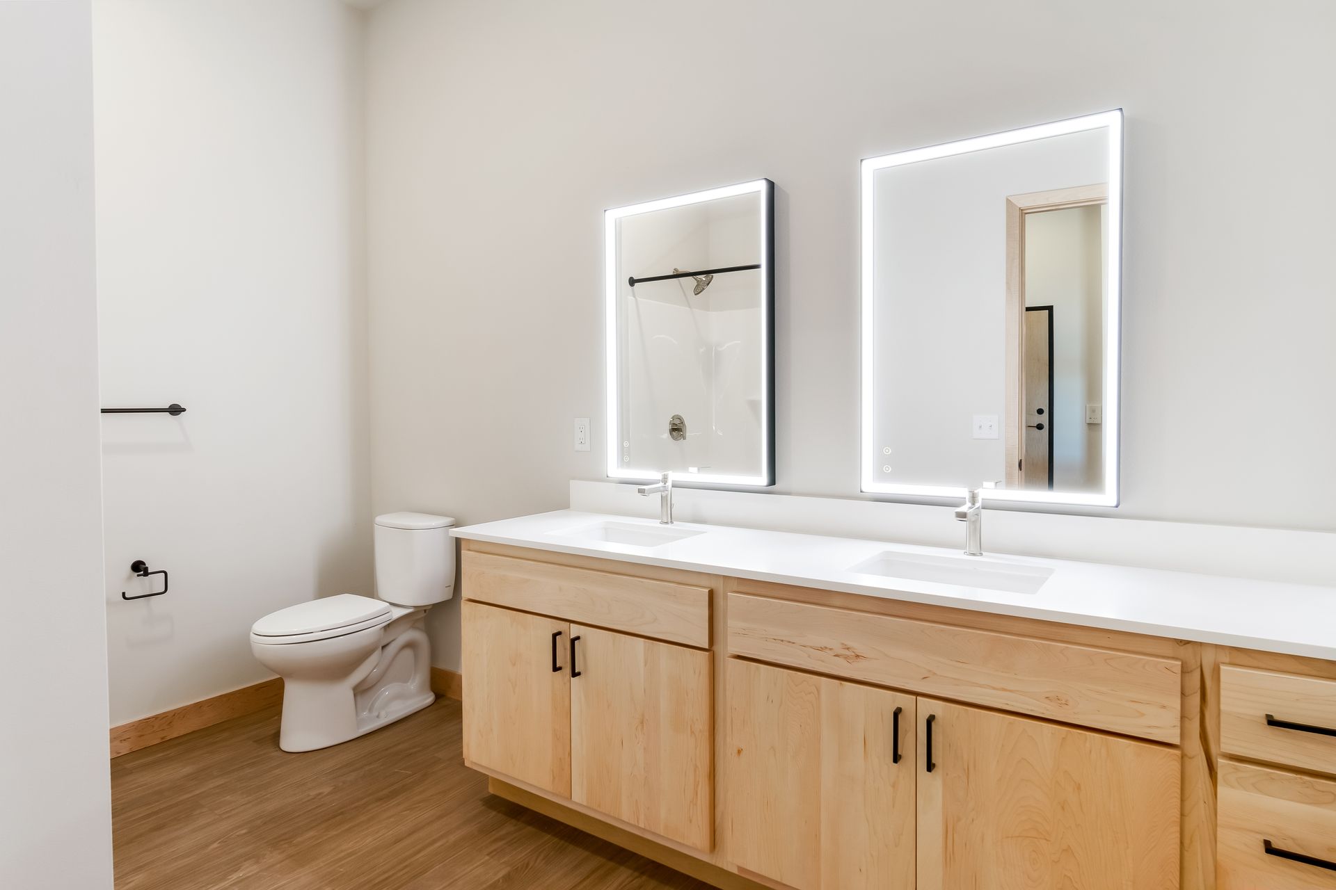 A bathroom with two sinks , a toilet , and two mirrors.