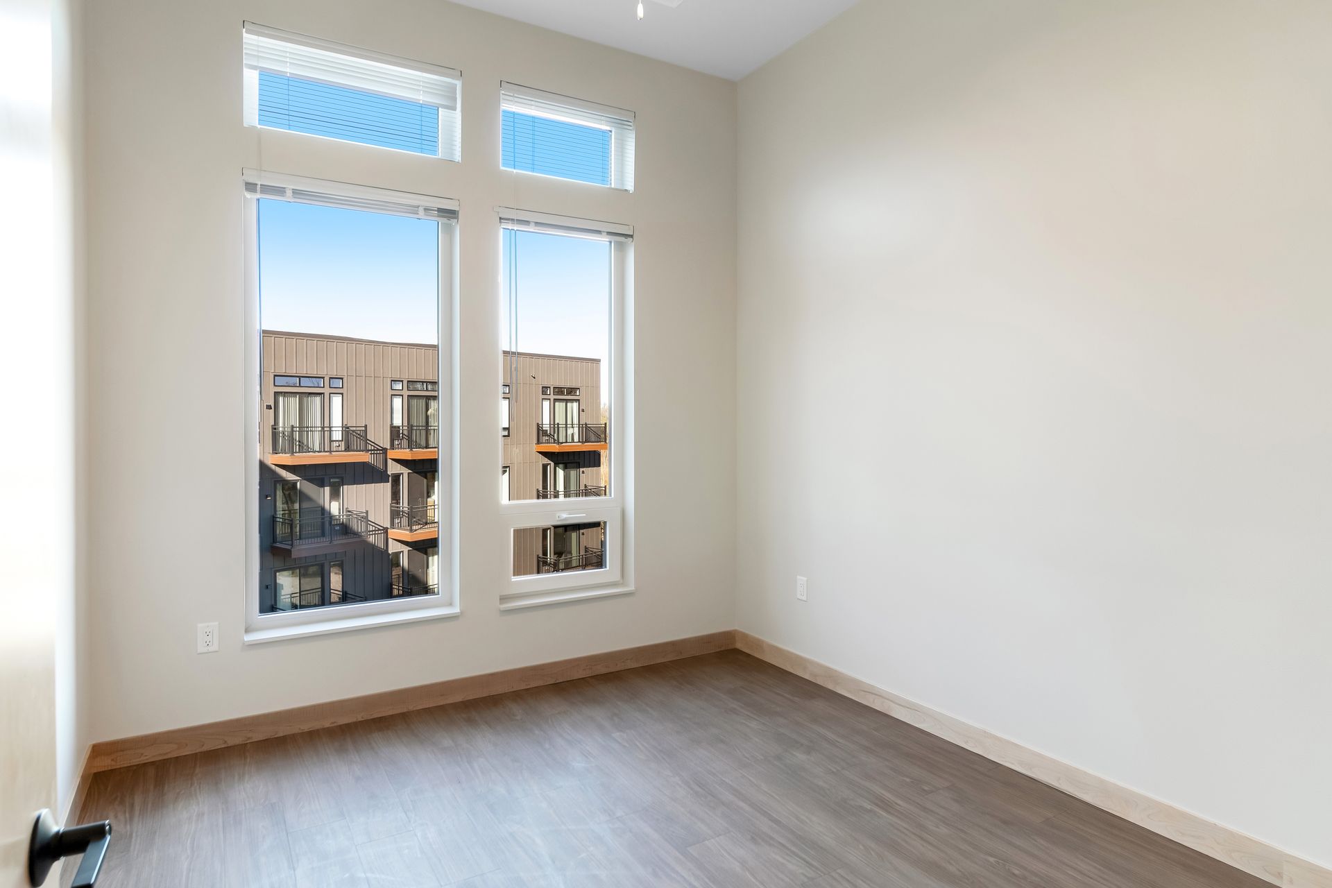 An empty room with two windows and a wooden floor.