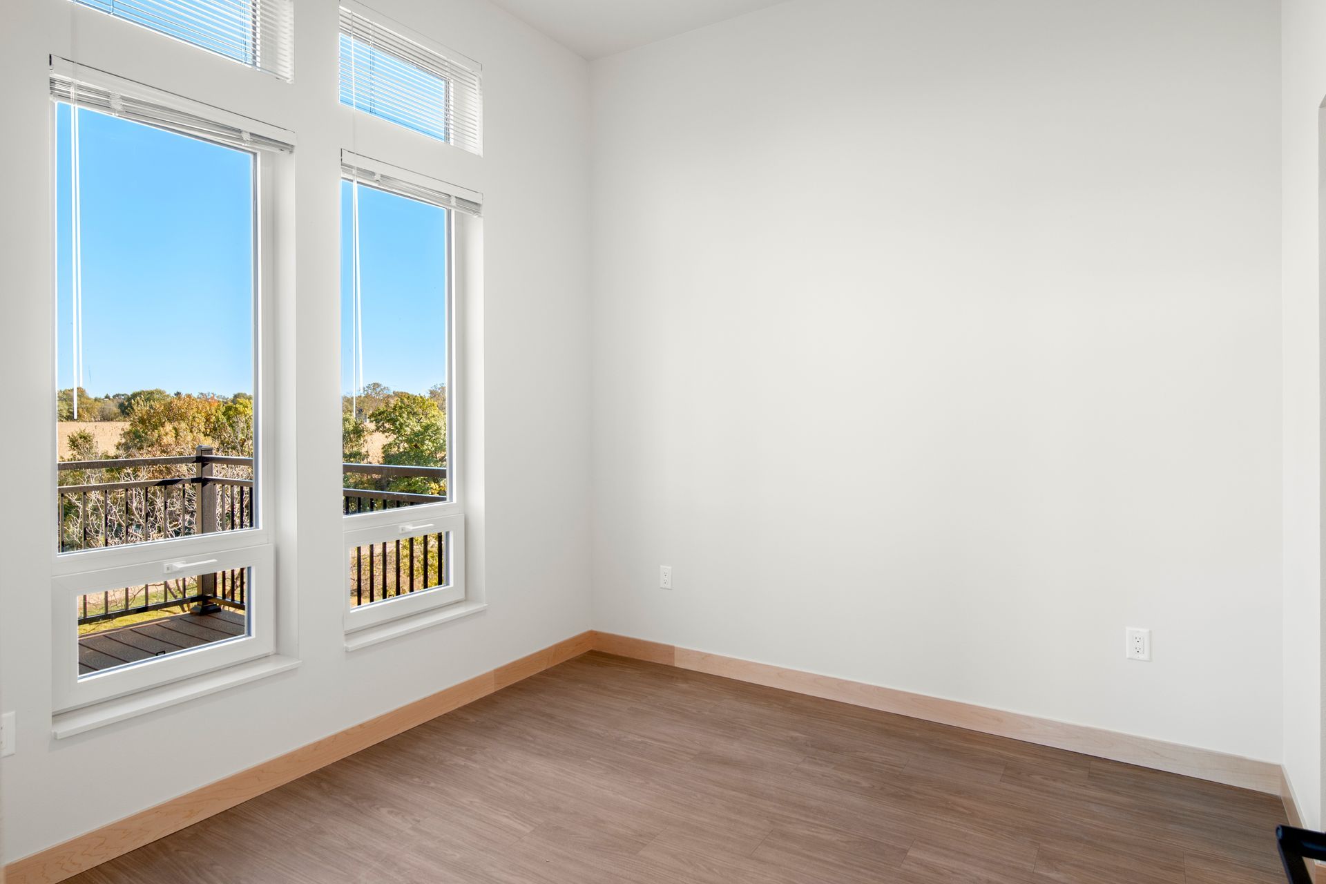 An empty room with two windows and a wooden floor.