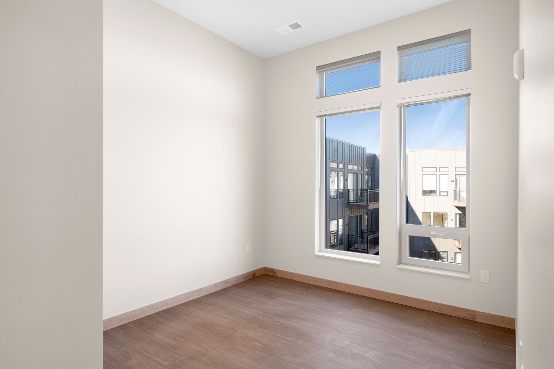 An empty room with two windows and a wooden floor.
