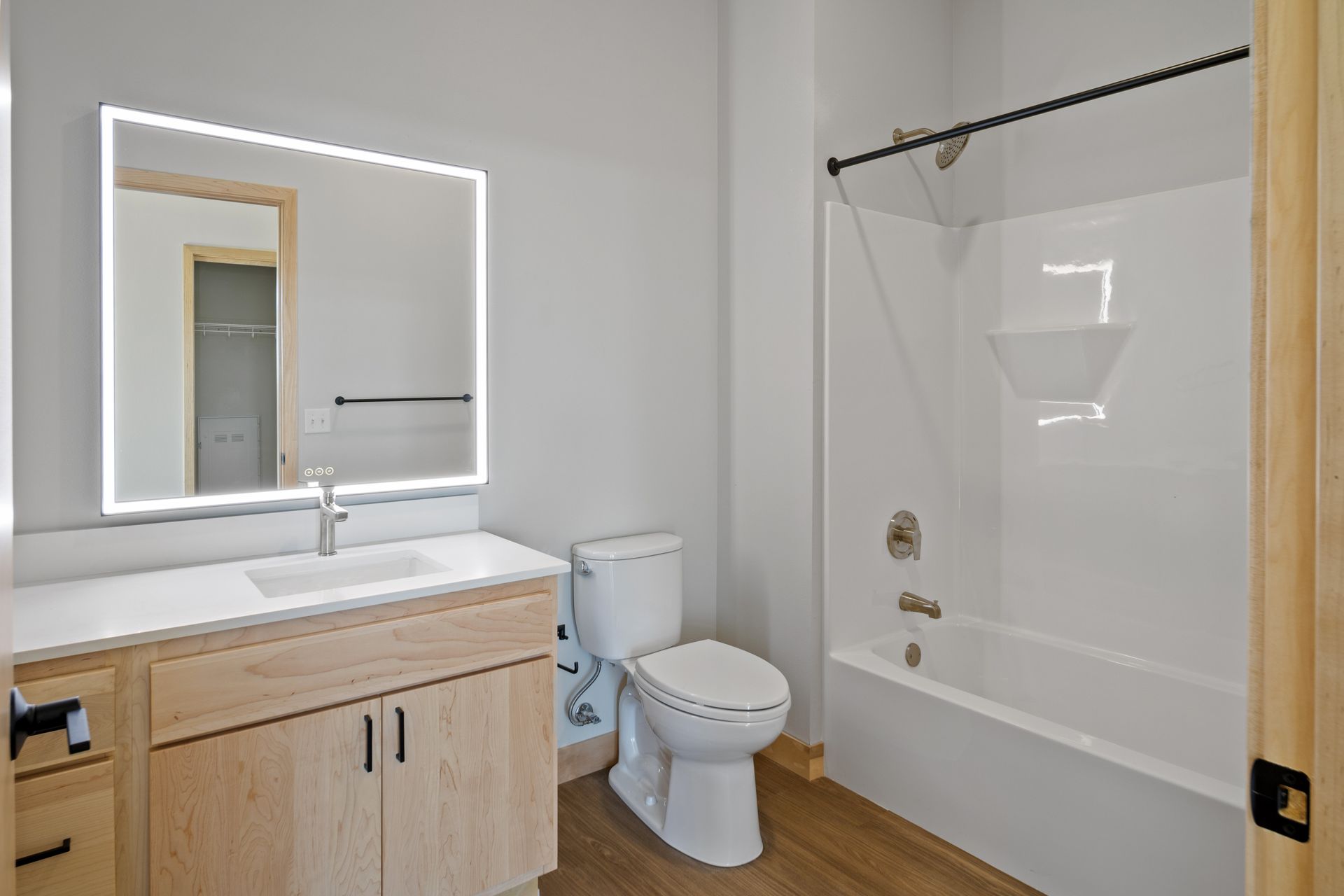 A bathroom with a toilet , sink , led mirror and bathtub.
