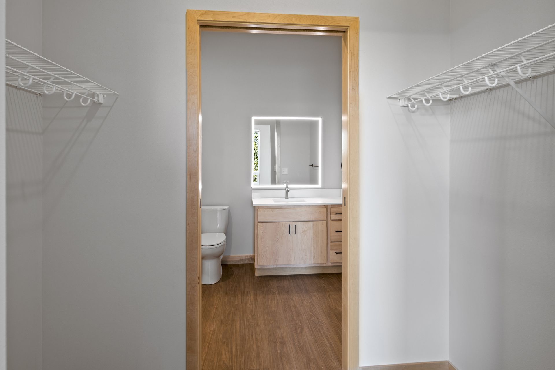 A walk-in closet leading to a bathroom with a toilet , sink and led mirror.