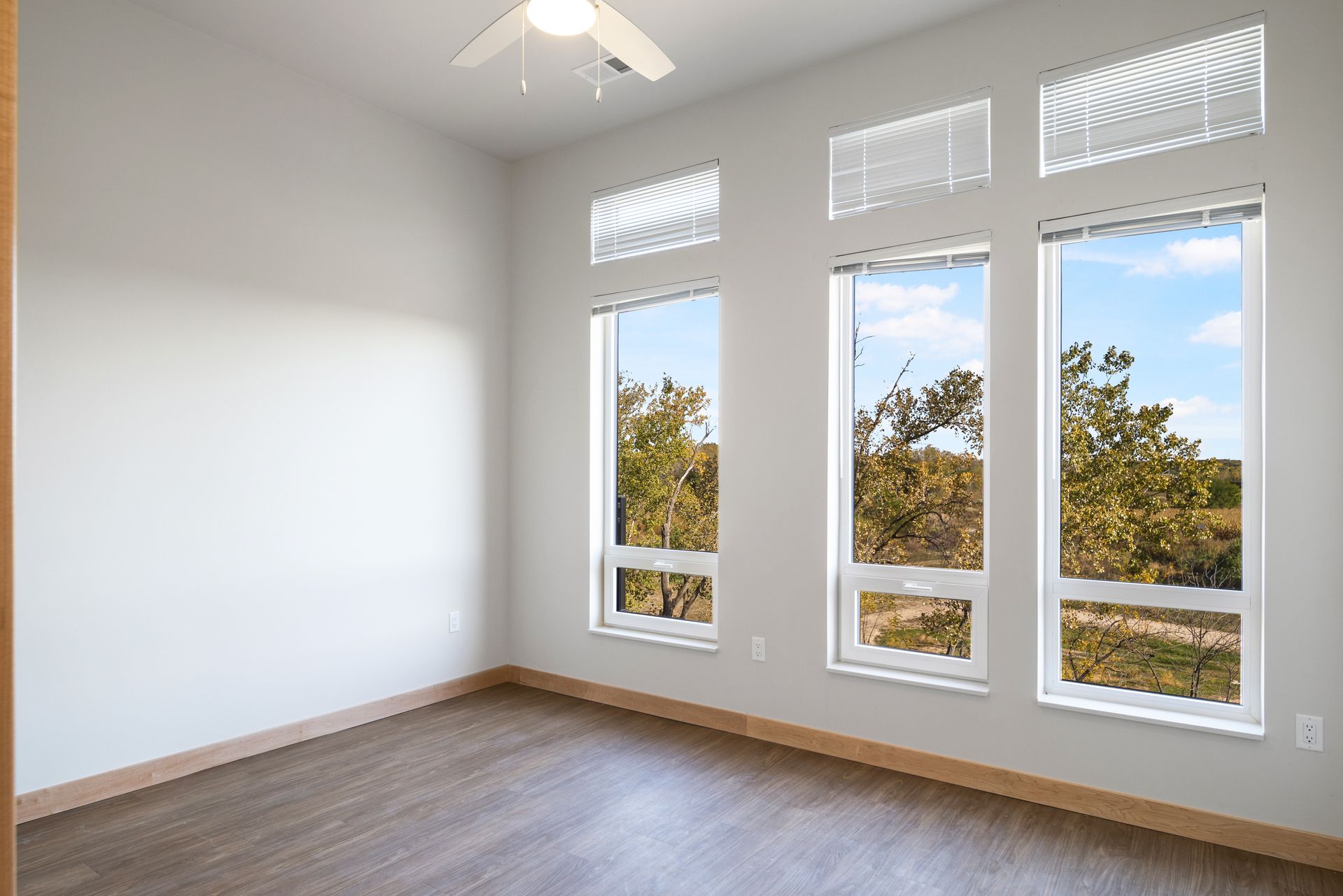 An large bedroom with three windows and a ceiling fan.