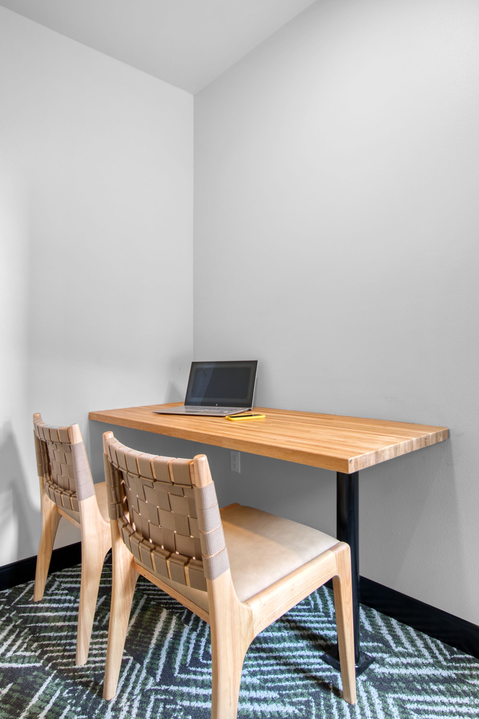 There is a desk with a laptop on it and two chairs.